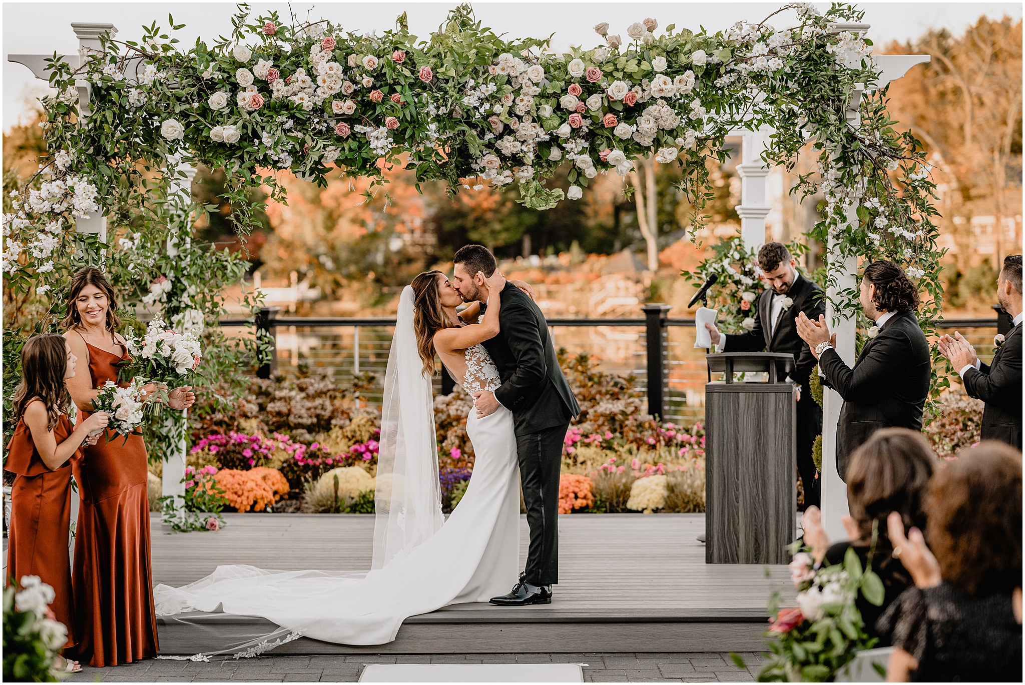 bride and groom kiss under floral arbor with white and pink flowers on patio at the Waters Edge at Centerport