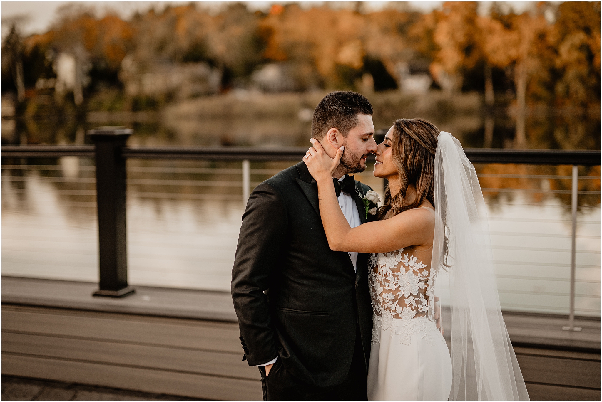 bride and groom lean to kiss standing on patio overlooking pond on Long Island