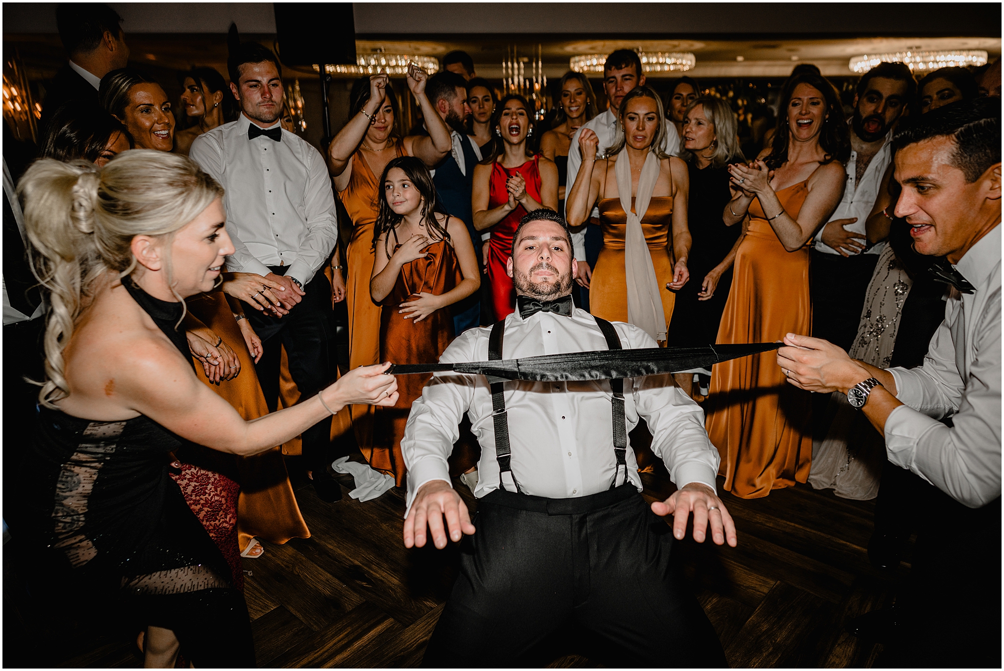 groom limbos under black cummerbund on dance floor during Long Island wedding reception