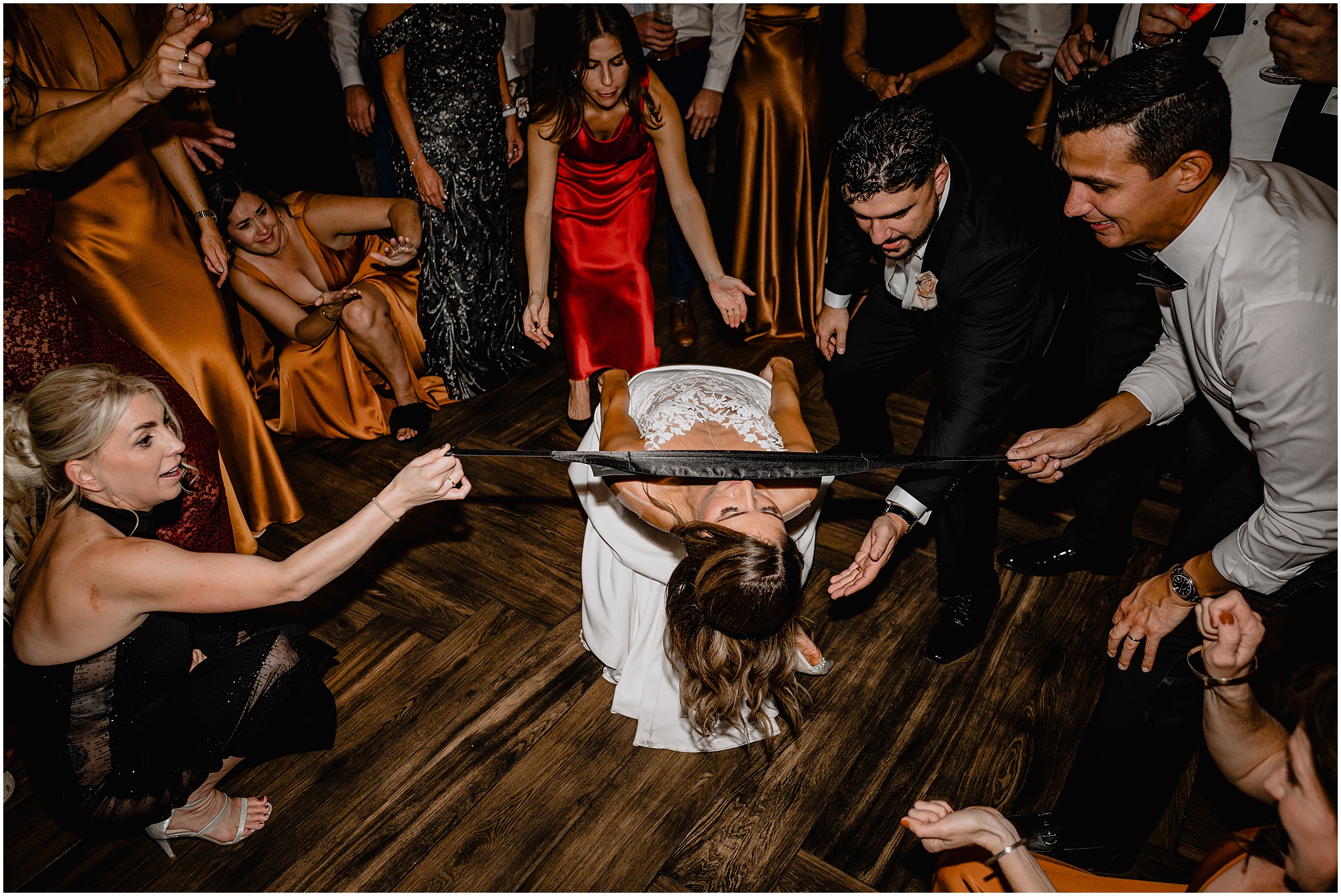 bride limbos under black cummerbund during Long Island wedding reception