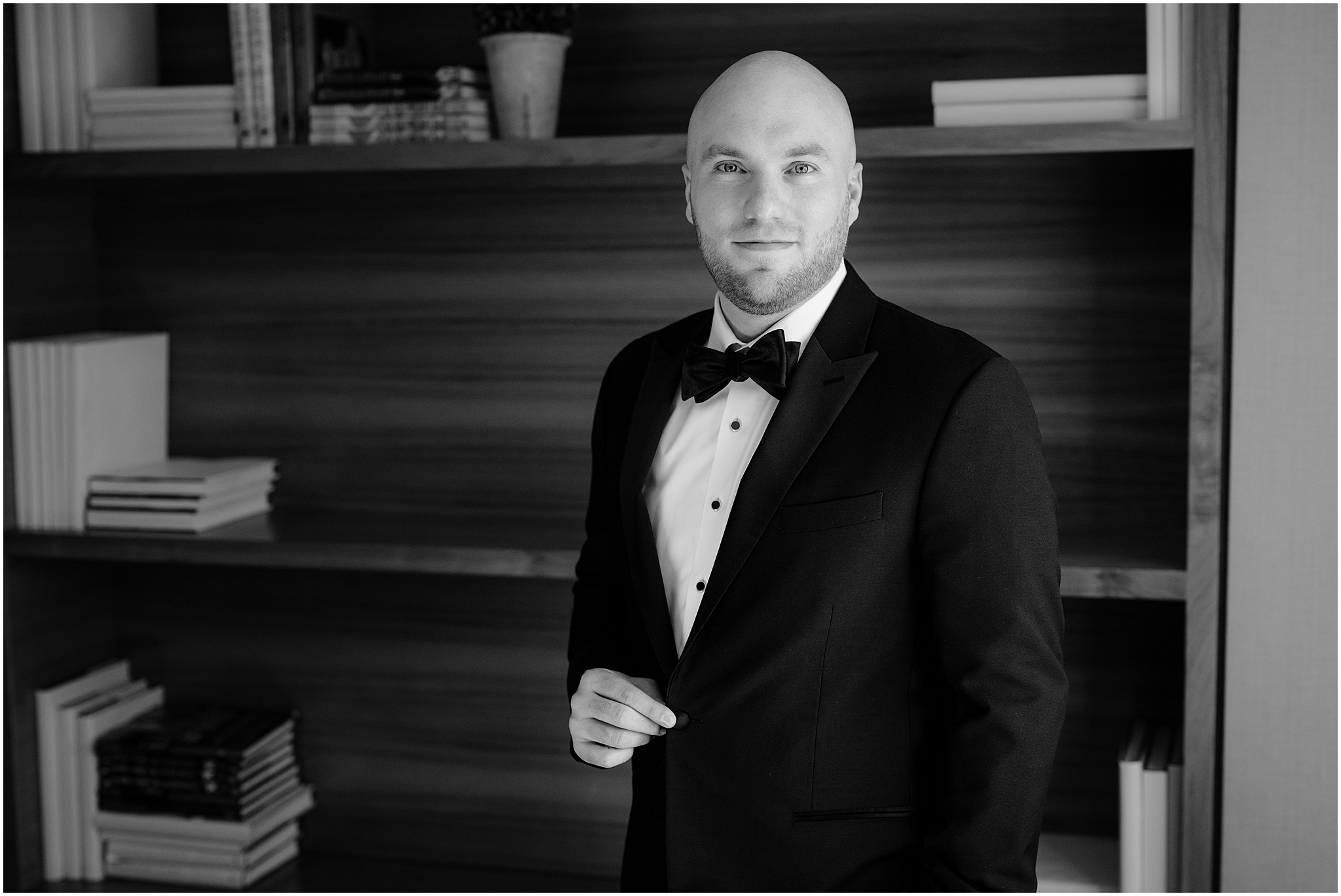 groom smiles holding lapel of suit jacket in library of home in Jersey City