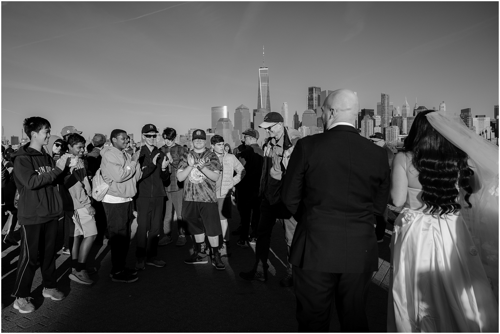 people clap as bride and groom walk alongside waterfront in New Jersey