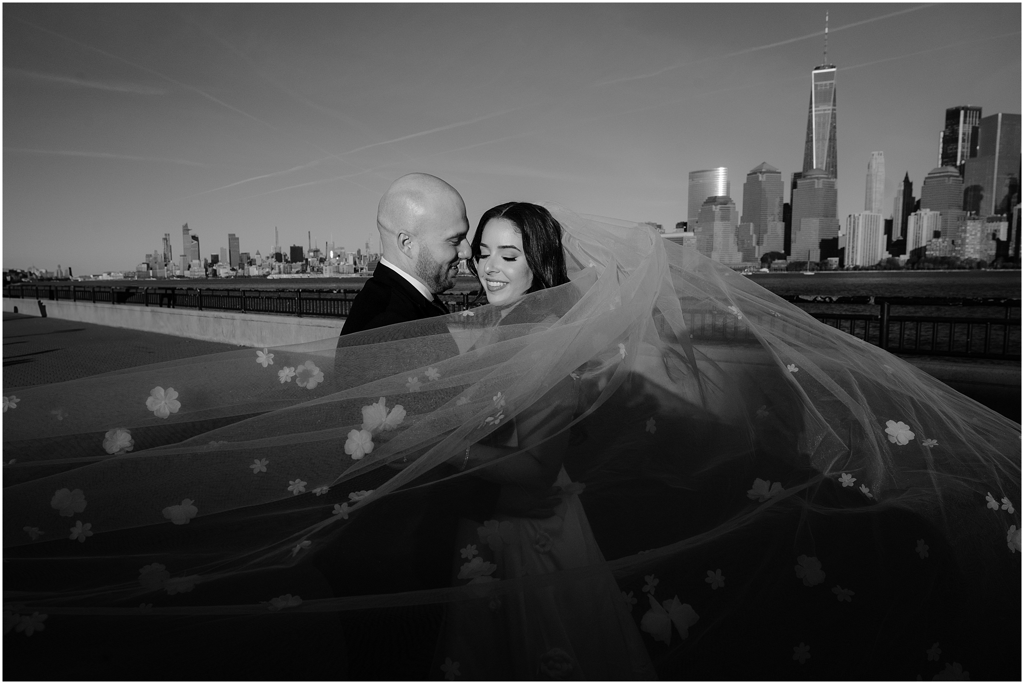 bride and groom hug with veil wrapped around them in front of NYC skyline 