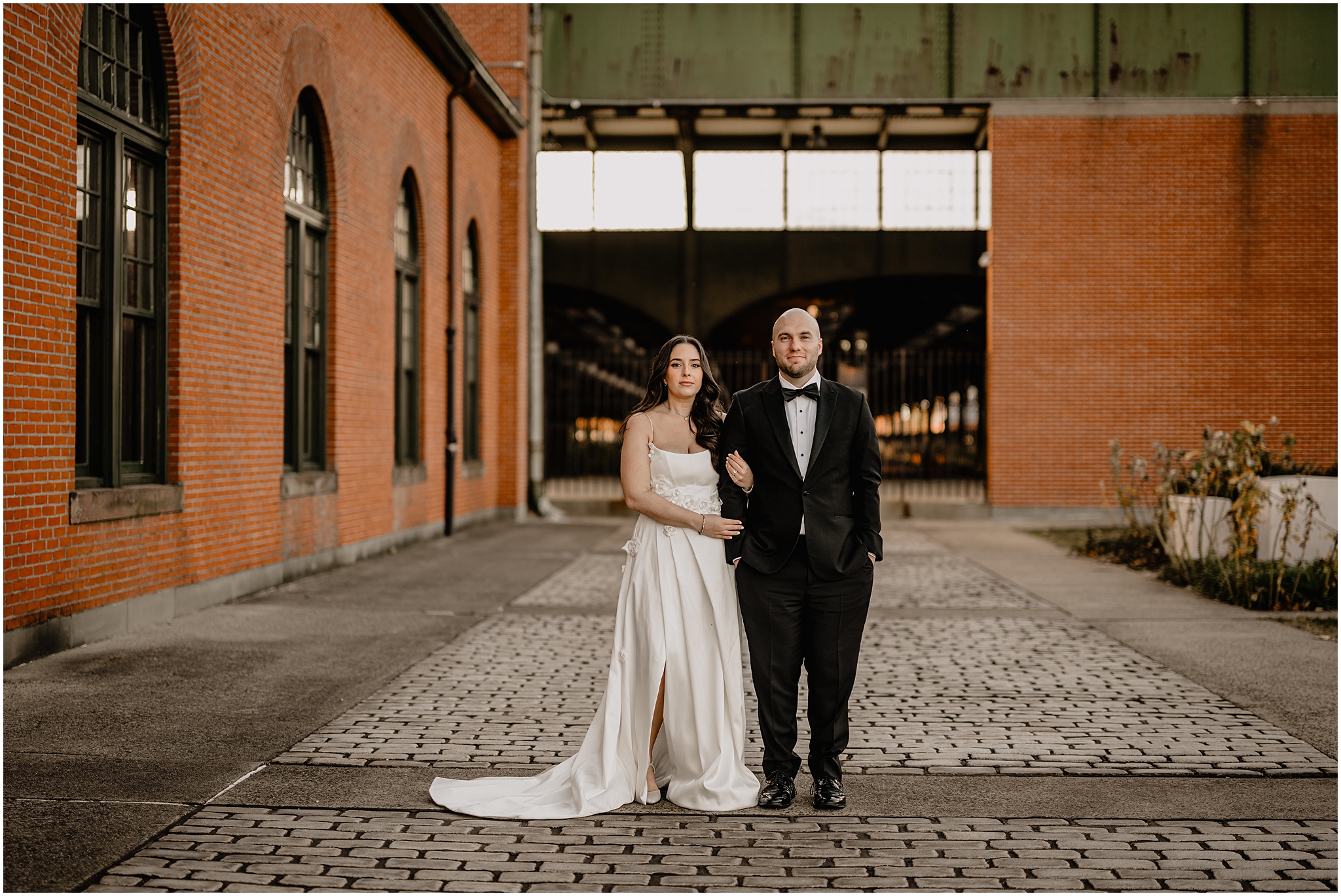 bride holds groom's arm in front of brick building in Jersey City