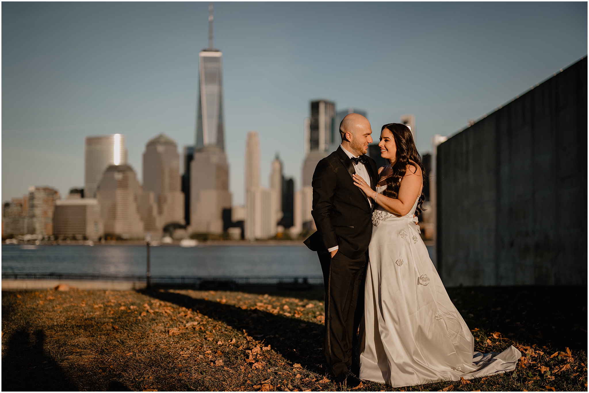 bride holds groom's lapel in front of Manhattan skyline in Jersey City
