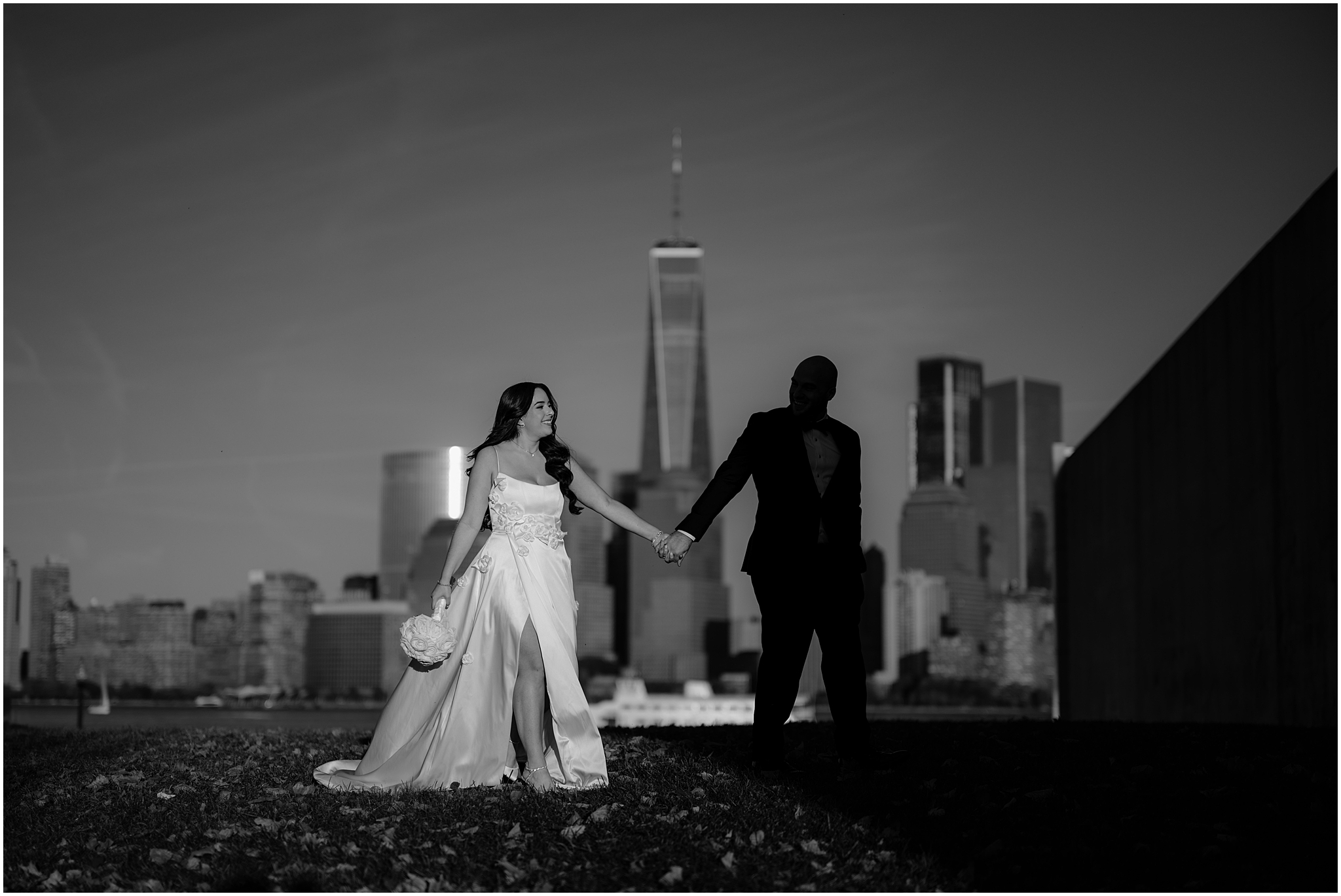 bride and groom hold hands walking on lawn in front of the Freedom Tower 