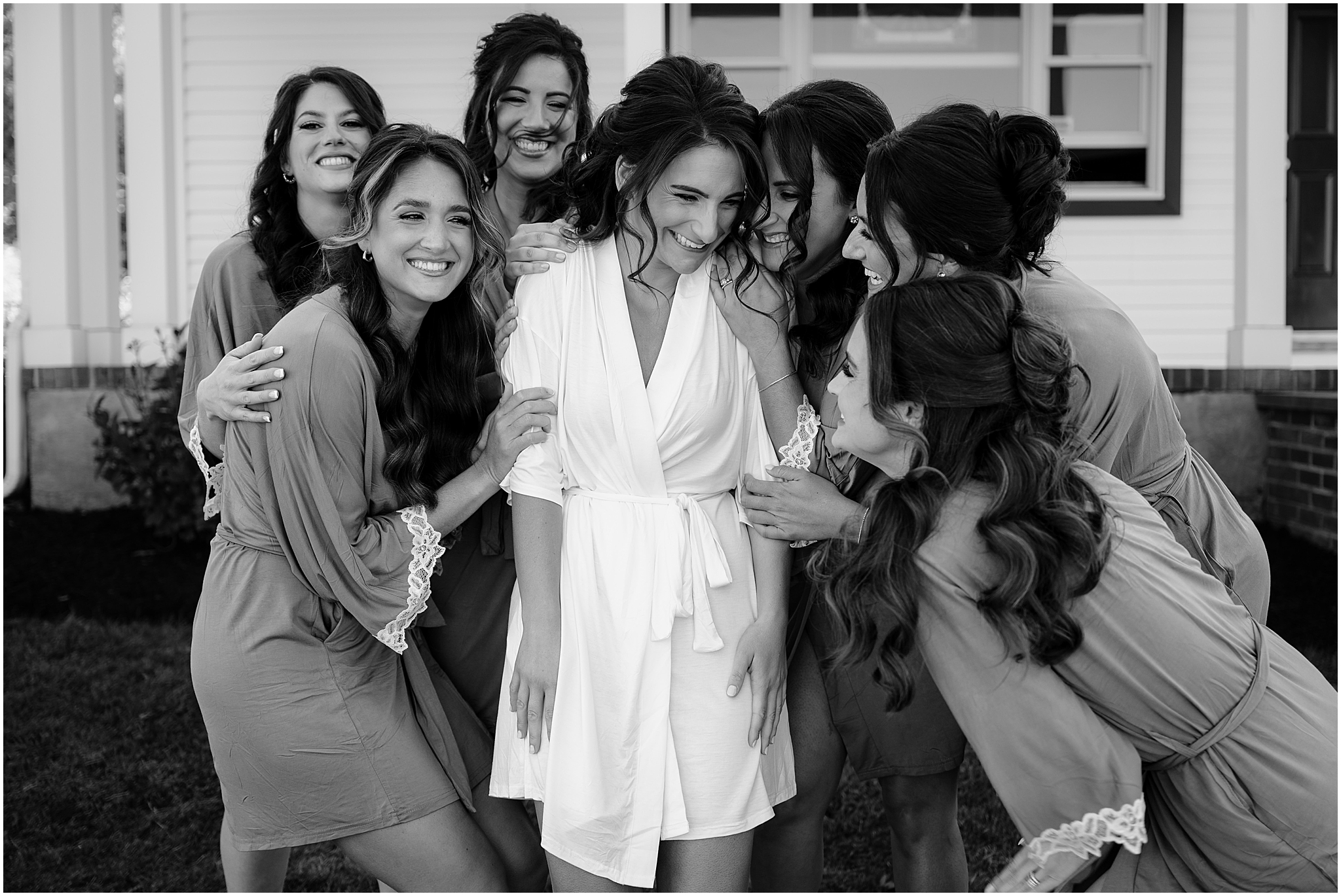 bridesmaids hug bride in matching robes outside The Shadowbrook at Shrewsbury