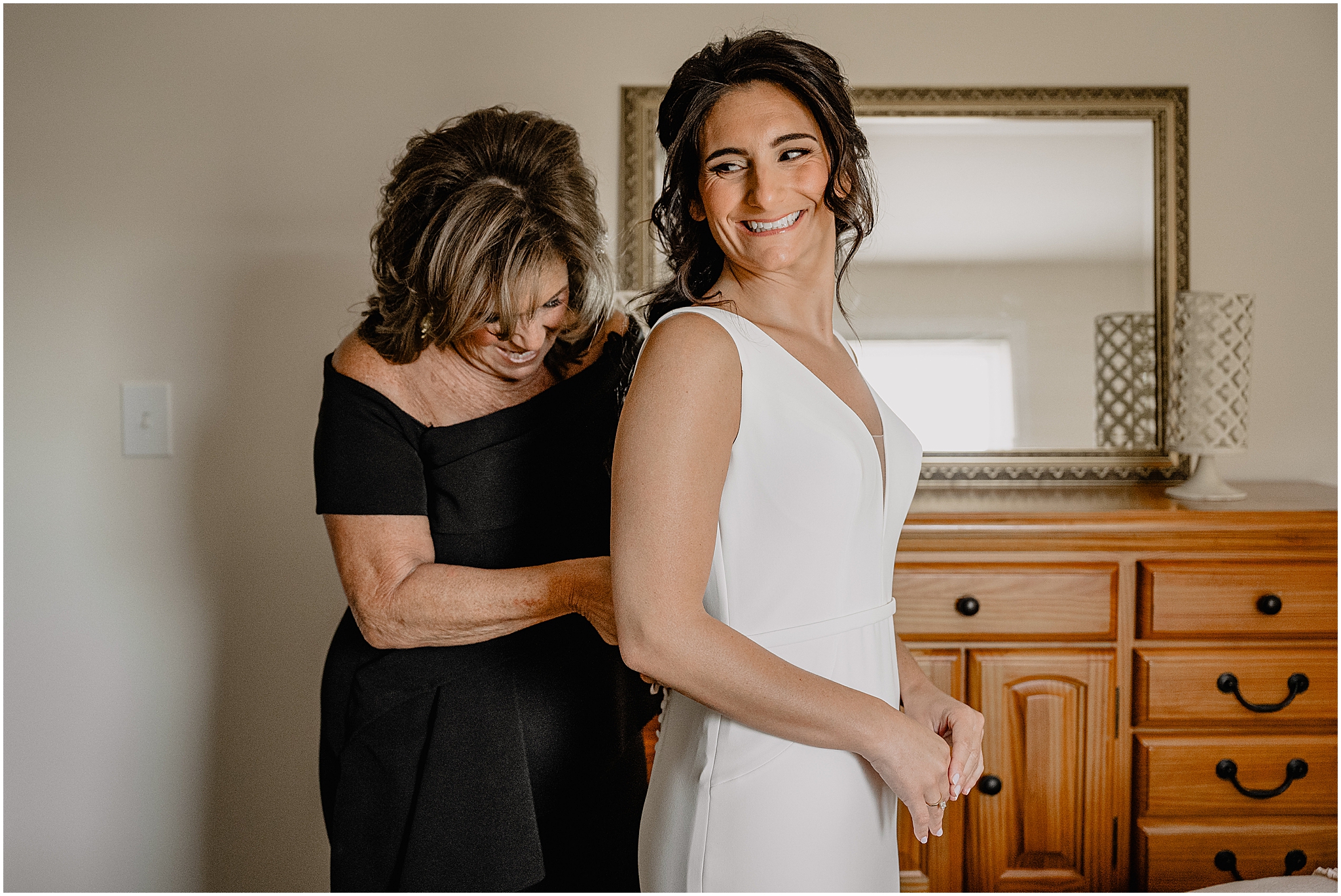 mother in black gown helps bride into wedding dress for NJ Wedding day