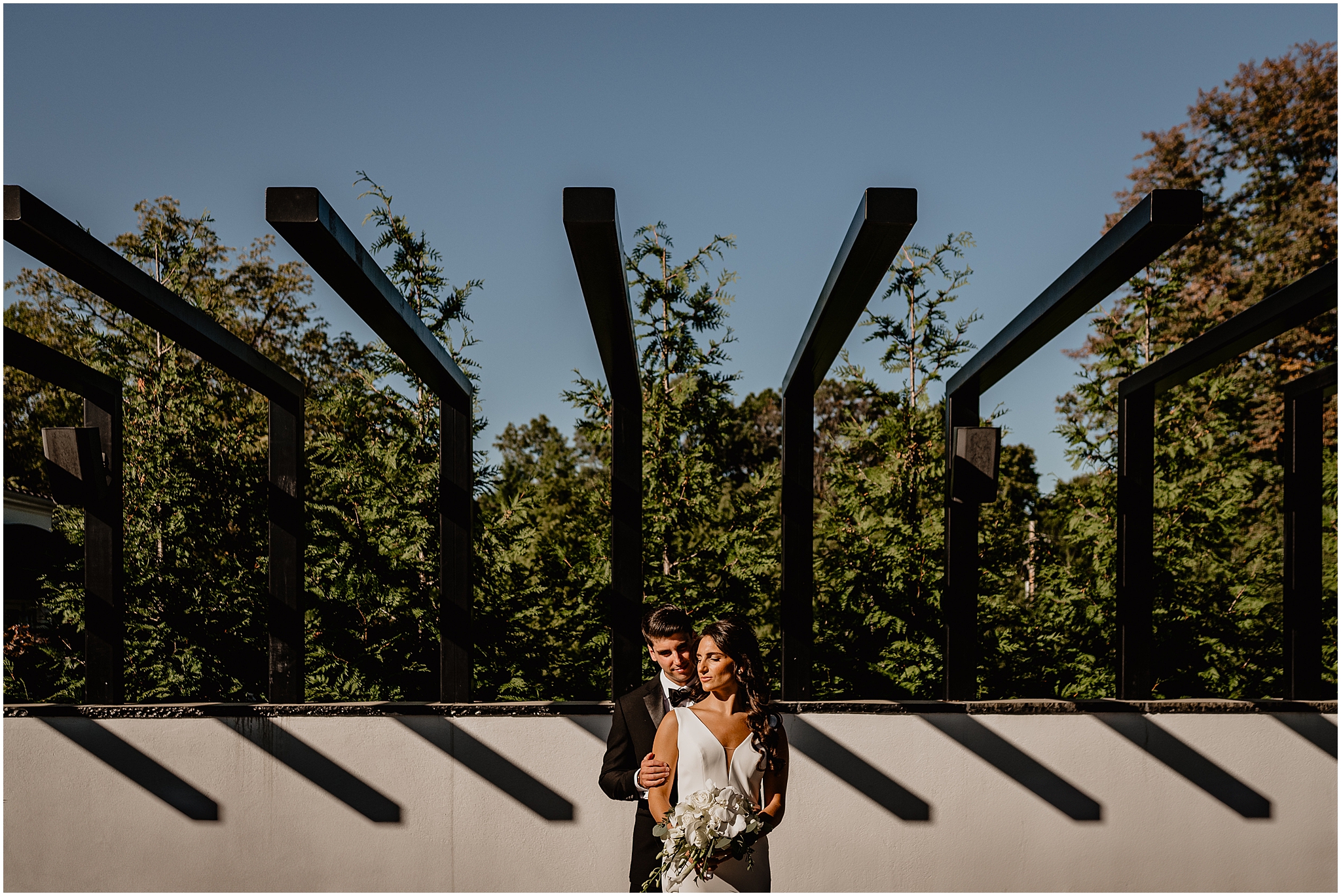 groom stands behind bride hugging her on outdoor patio at The Shadowbrook at Shrewsbury