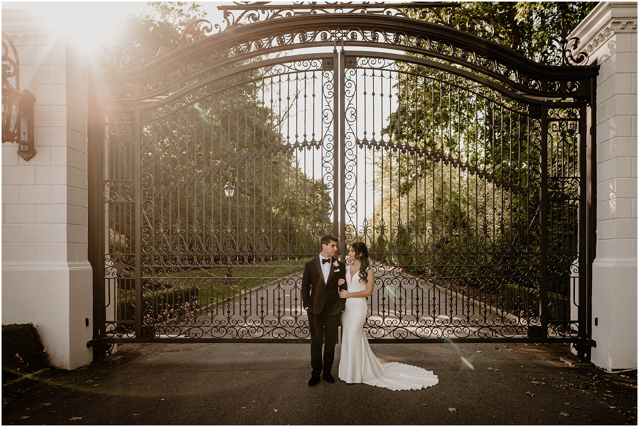 bride holds groom's arm standing in front of black iron gate at The Shadowbrook at Shrewsbury
