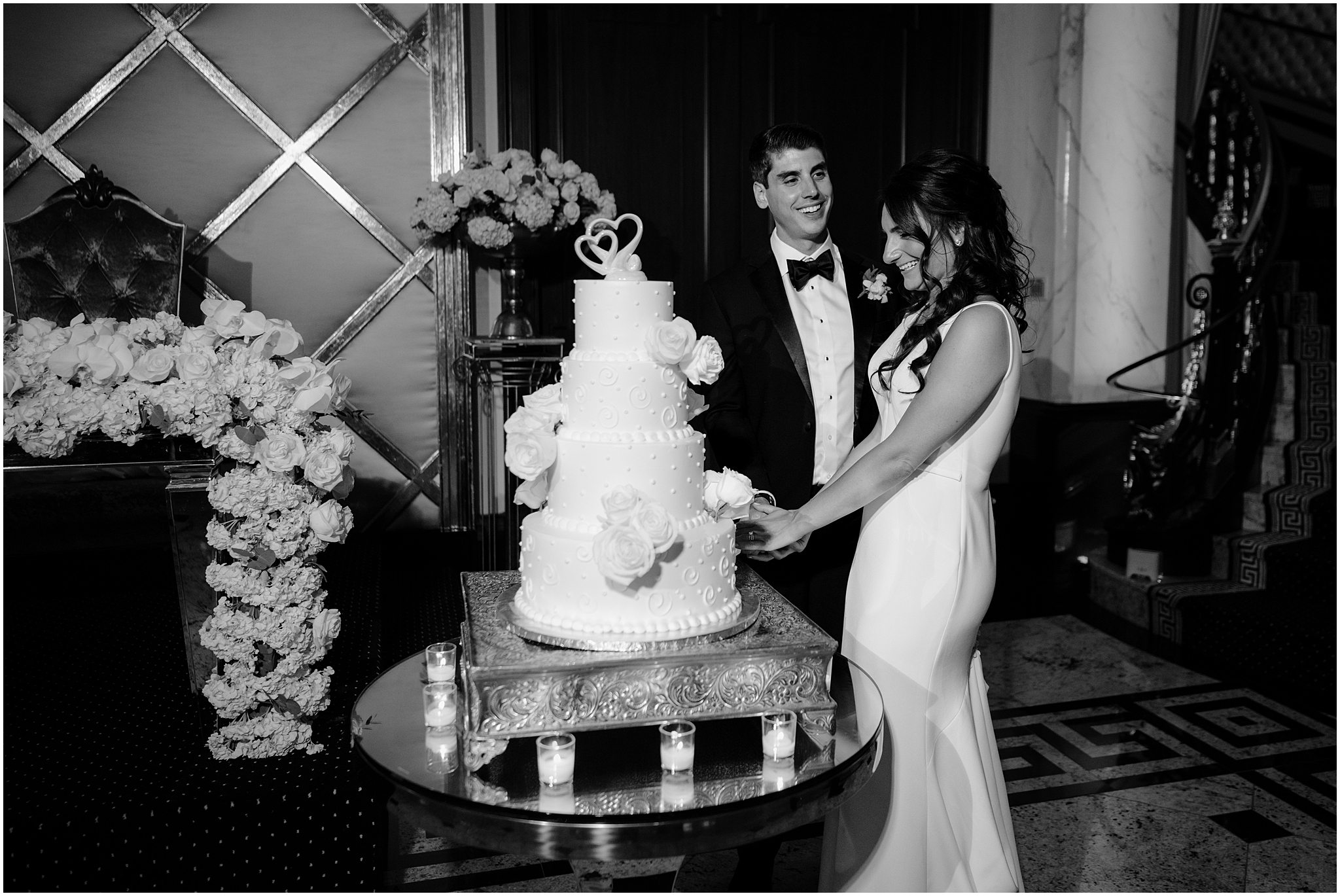 bride and groom cut traditional tiered wedding cake with white rose details during New Jersey wedding reception 