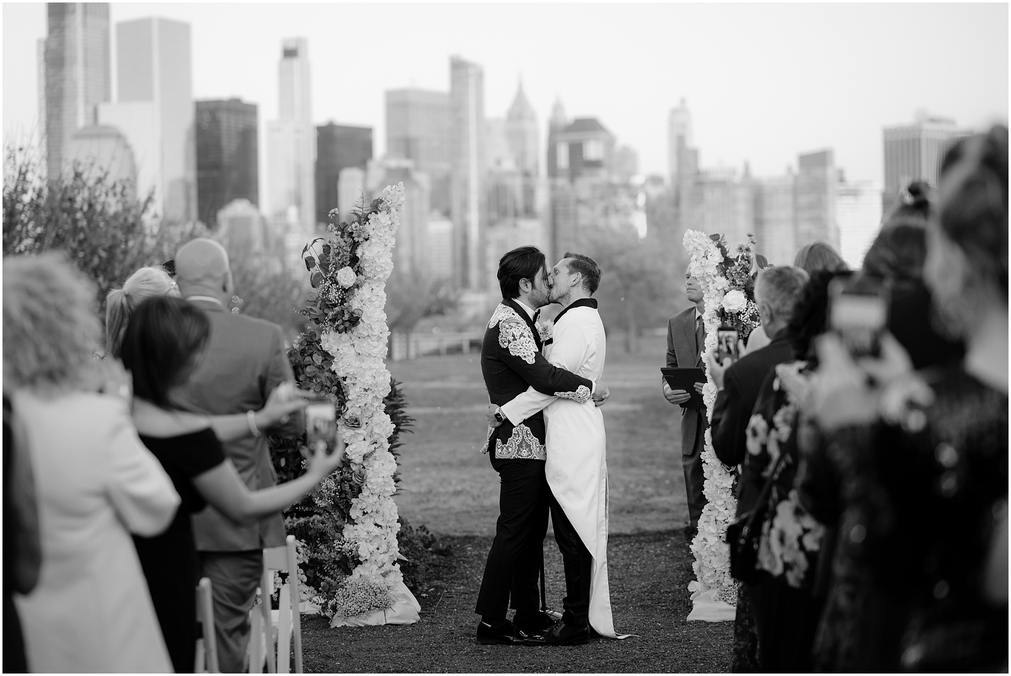 two grooms kiss between white floral arrangements on ceremony site at the Liberty House in Jersey City