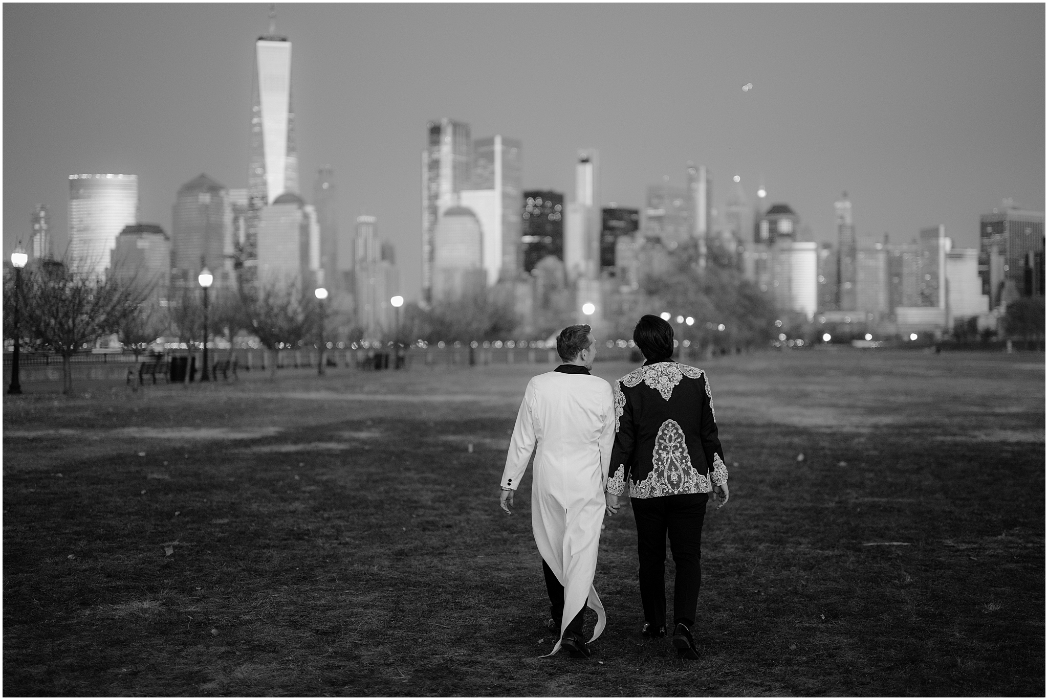 men in custom suits walks towards Manhattan skyline in Jersey City park