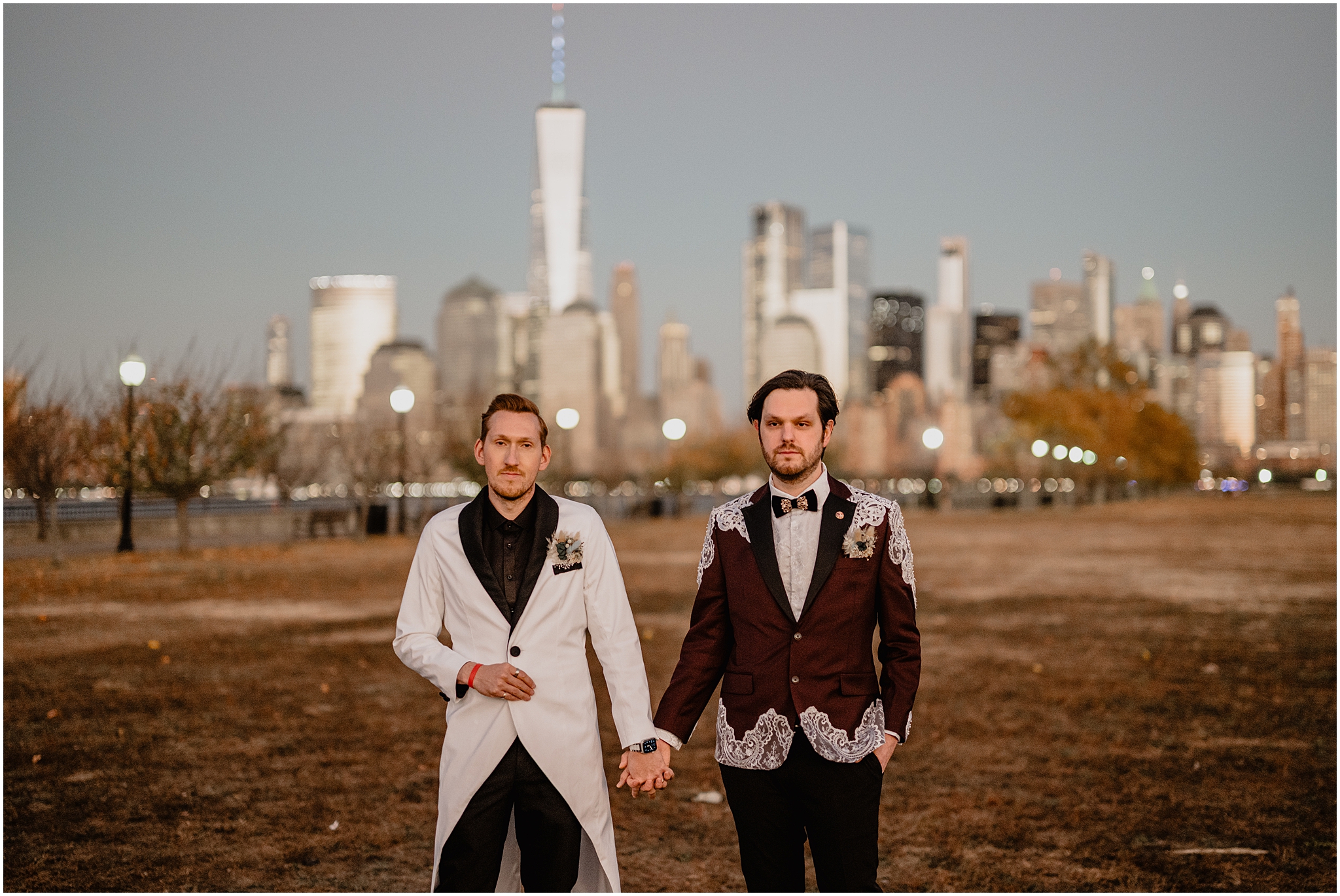 grooms hold hands walking in front of Manhattan skyline on fall wedding day