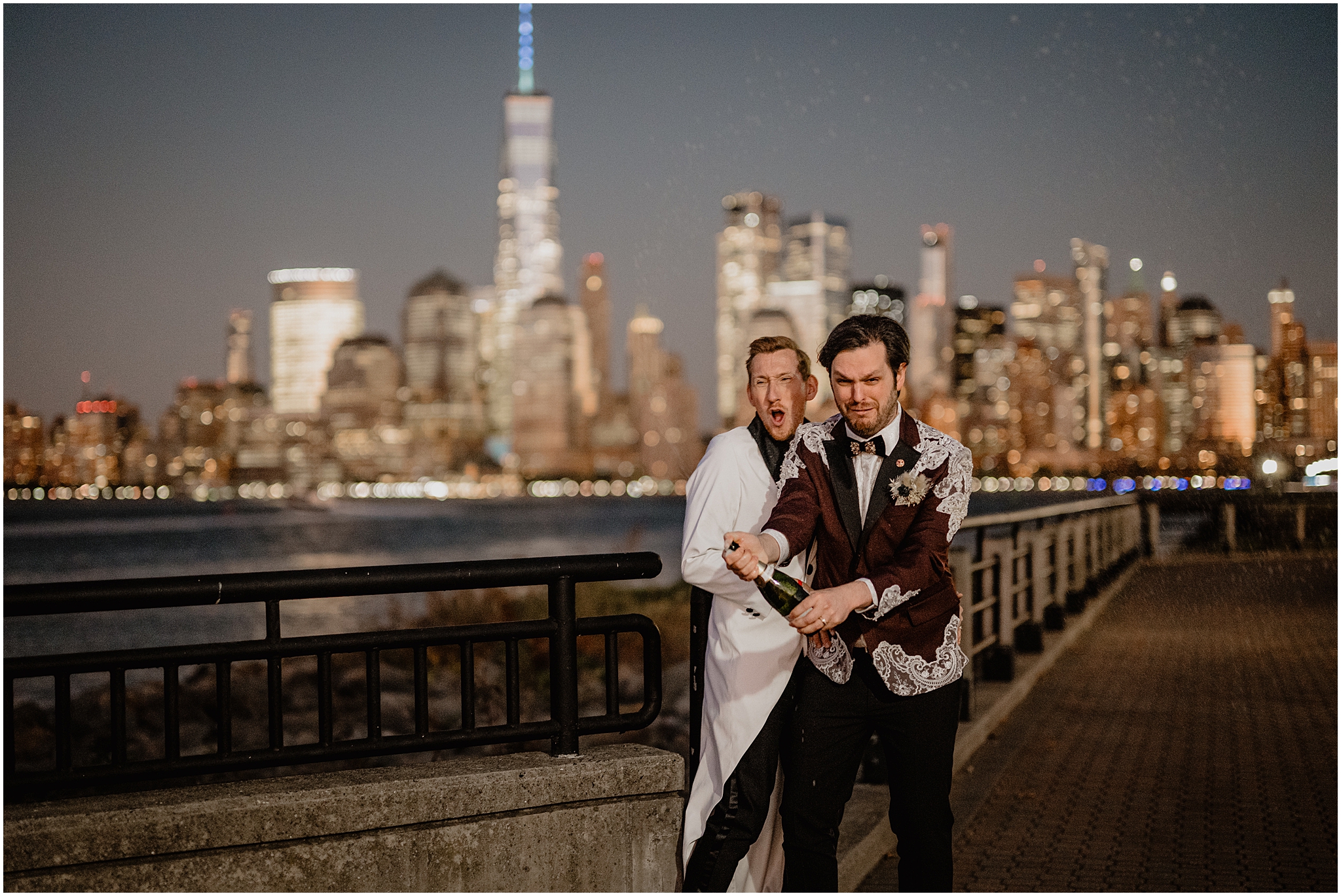 couple pops champagne in front of NYC skyline at night 