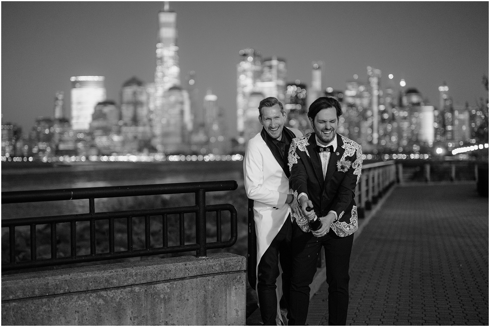 man pops champagne with husband behind him in front of NYC skyline 