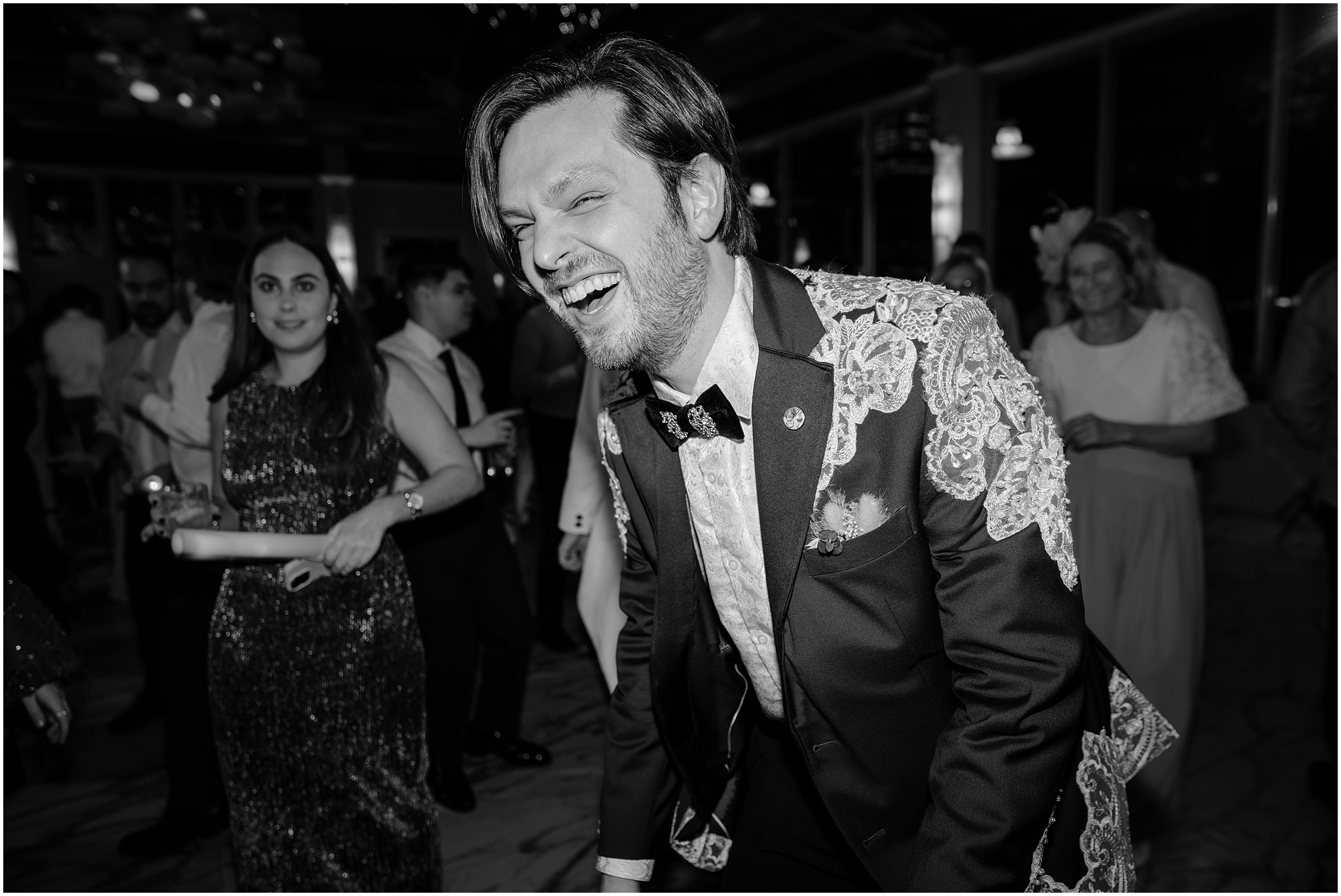 groom laughs in custom suit jacket with lace on the shoulders during wedding reception at the Liberty House in Jersey City