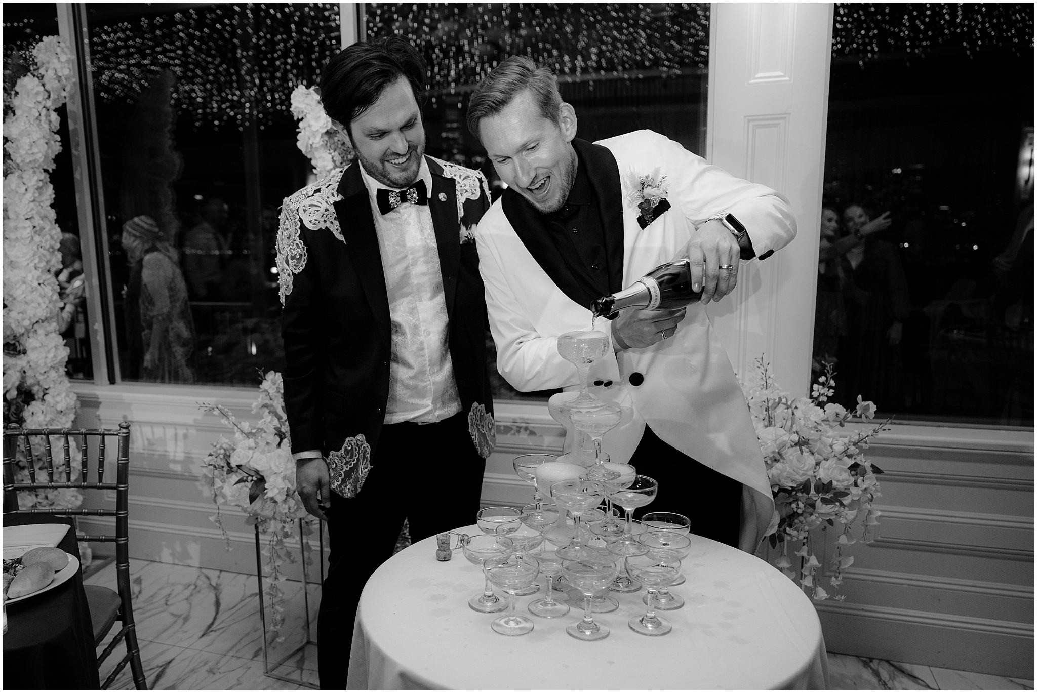 groom in white suit jacket pours champagne on tower at reception at the Liberty House in Jersey City