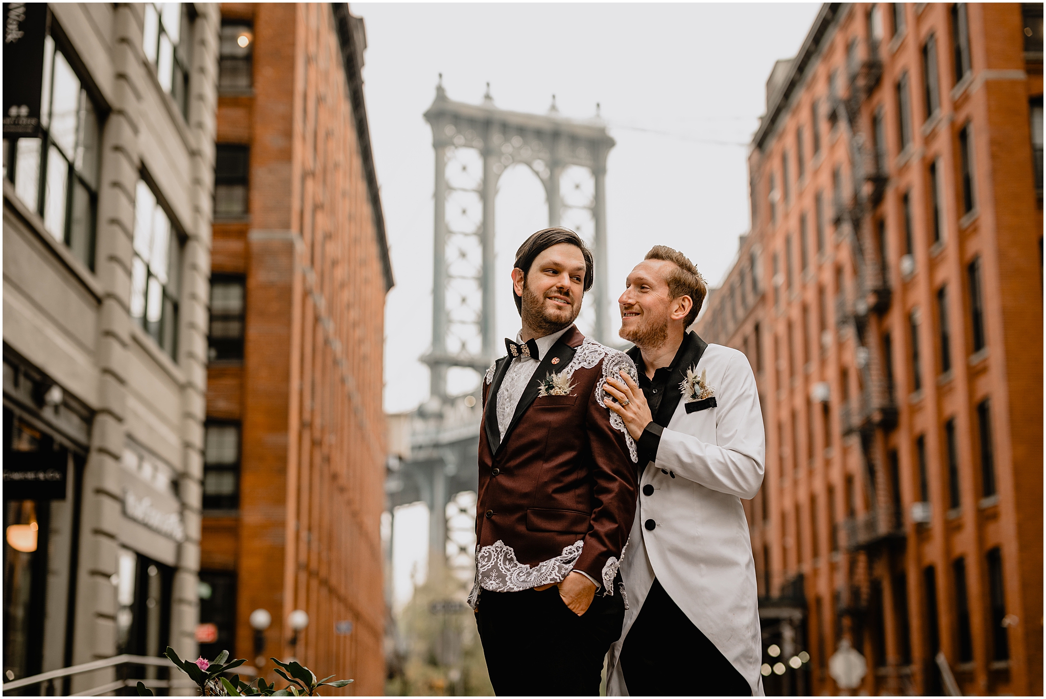 groom in white suit jacket hugs groom in burgundy and white lace suit jacket in DUMBO