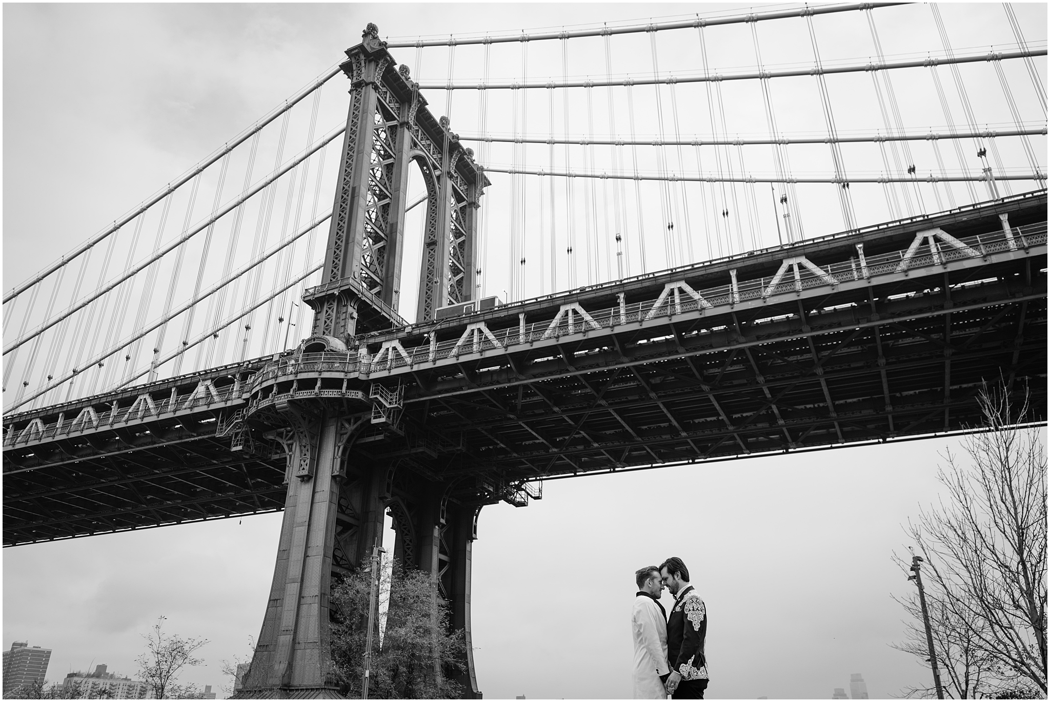two grooms hug under Brooklyn Bridge in New York City 