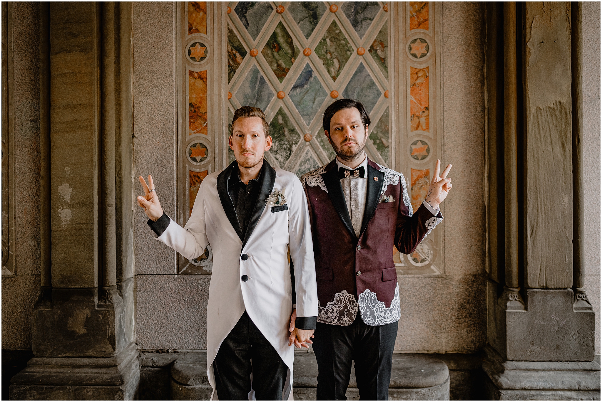 grooms hold hand making peace signs in front of colorful mural in Jersey City
