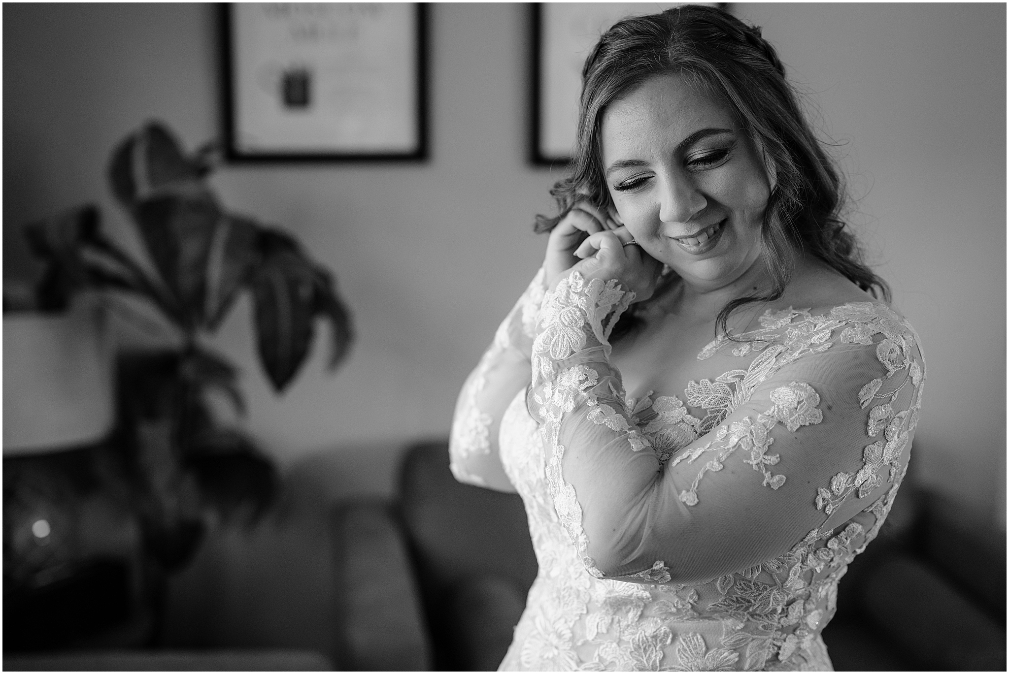 bride puts earrings on wearing wedding dress with lace sleeves in home