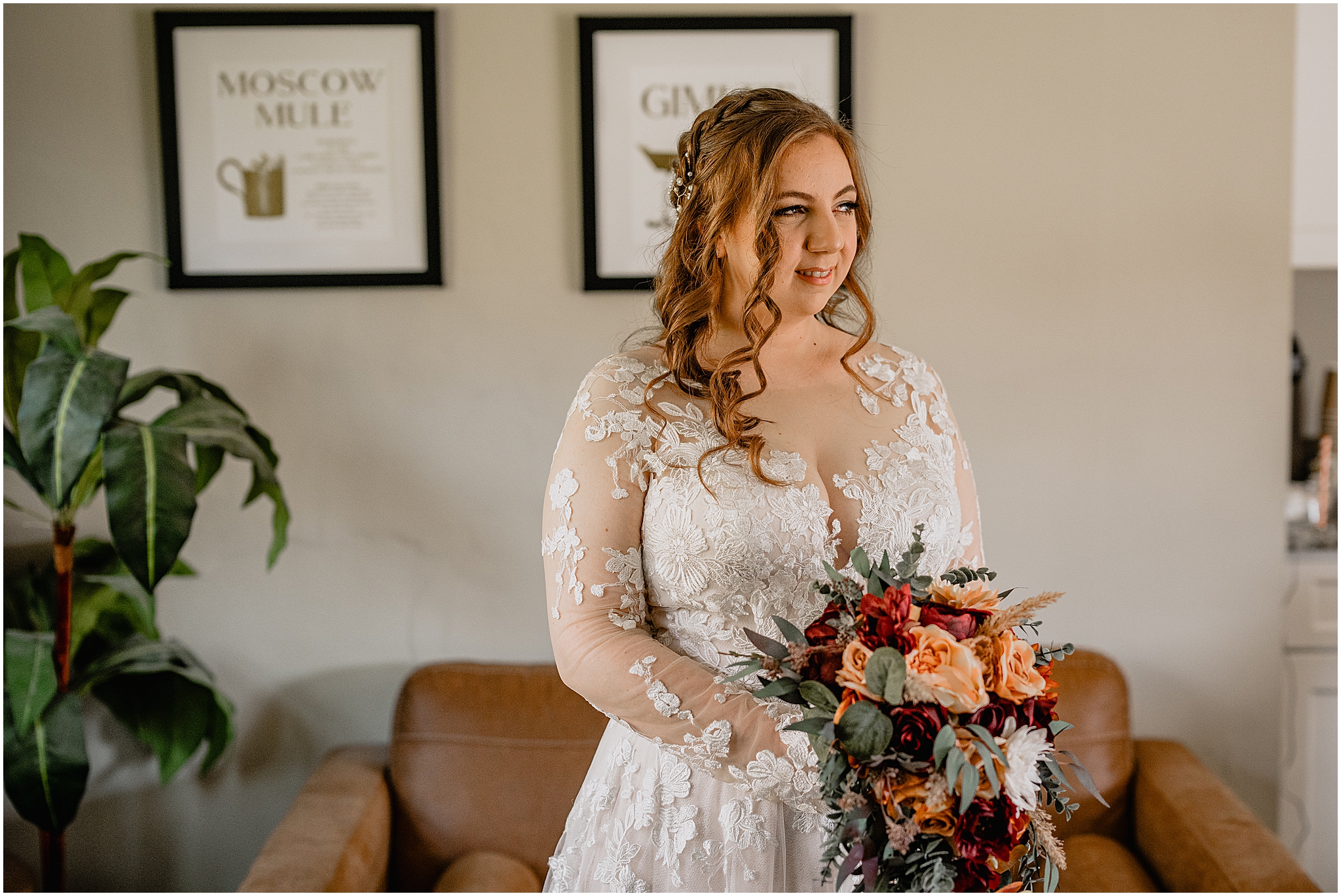 blonde bride smiles holding bouquet of orange and red flowers in living room of New Jersey home