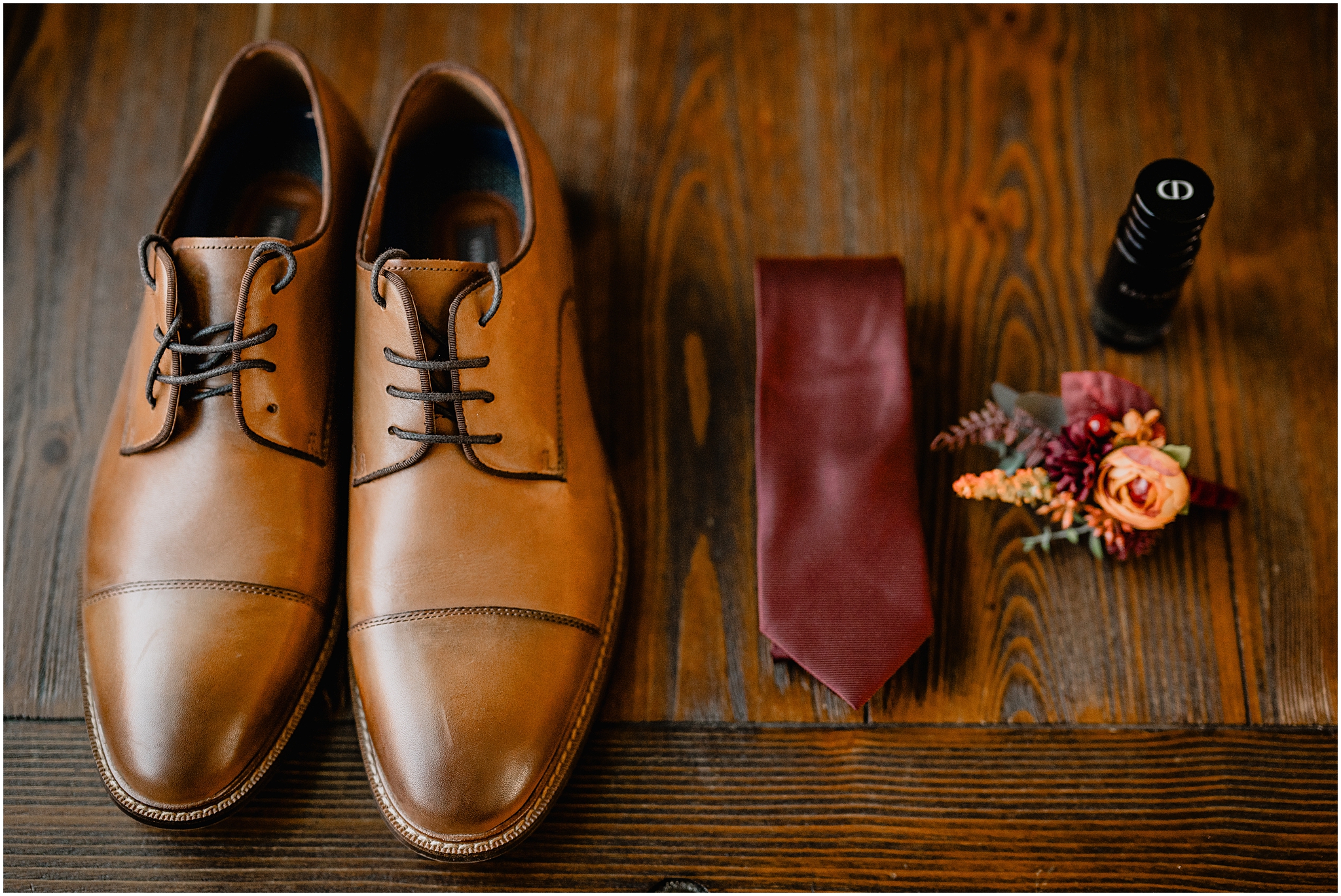 groom's brown shoes and burgundy tie with fall boutonnière on wooden floor 