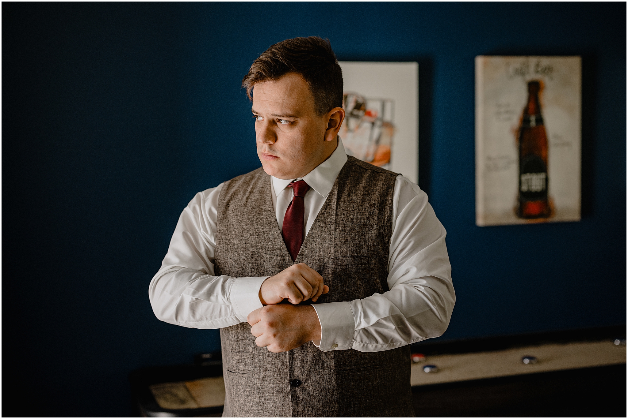 groom pulls cufflinks in front of blue wall in billiards room at the Barn at Perona Farms
