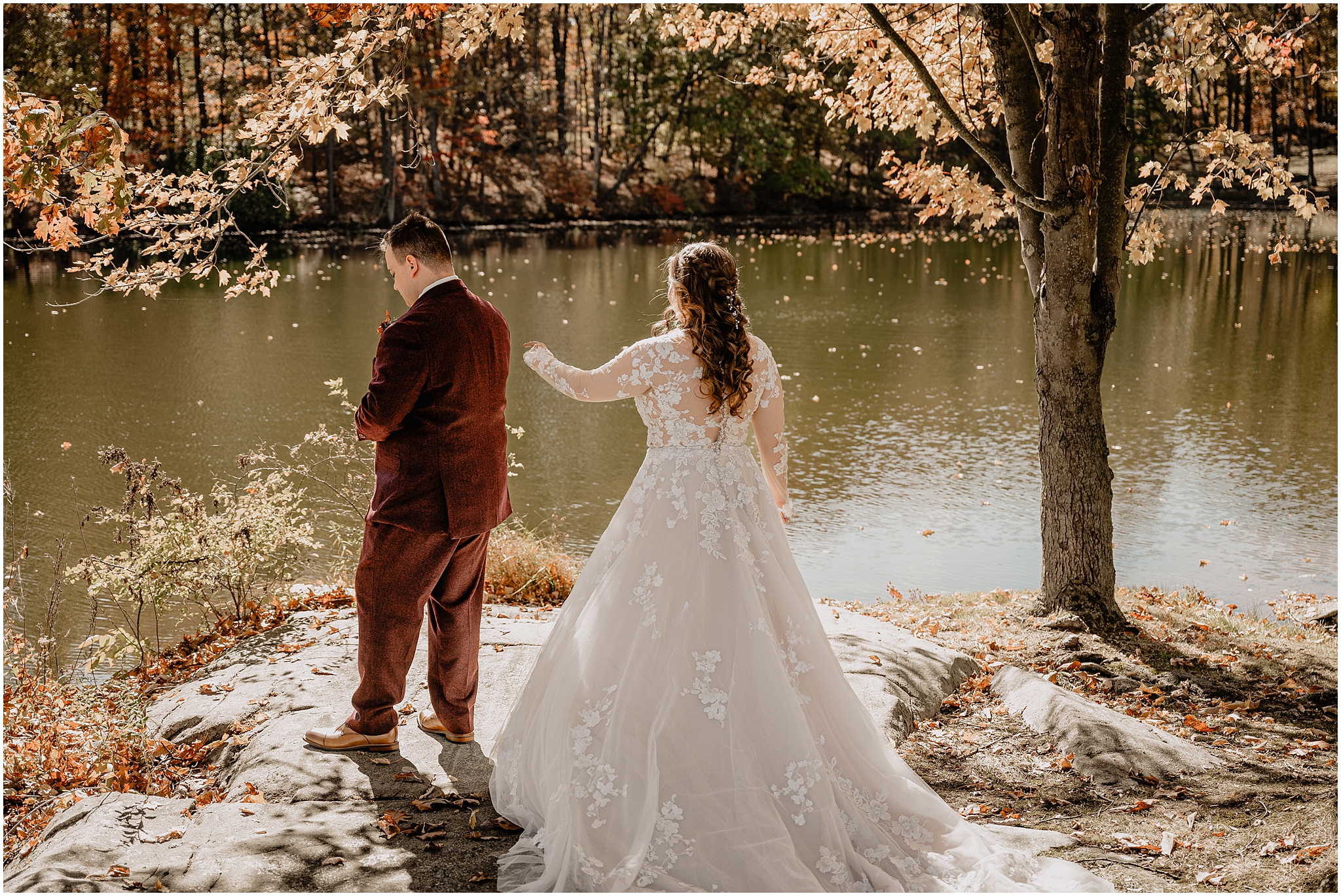 bride lifts arm to reach for groom during first look by pond at the Barn at Perona Farms