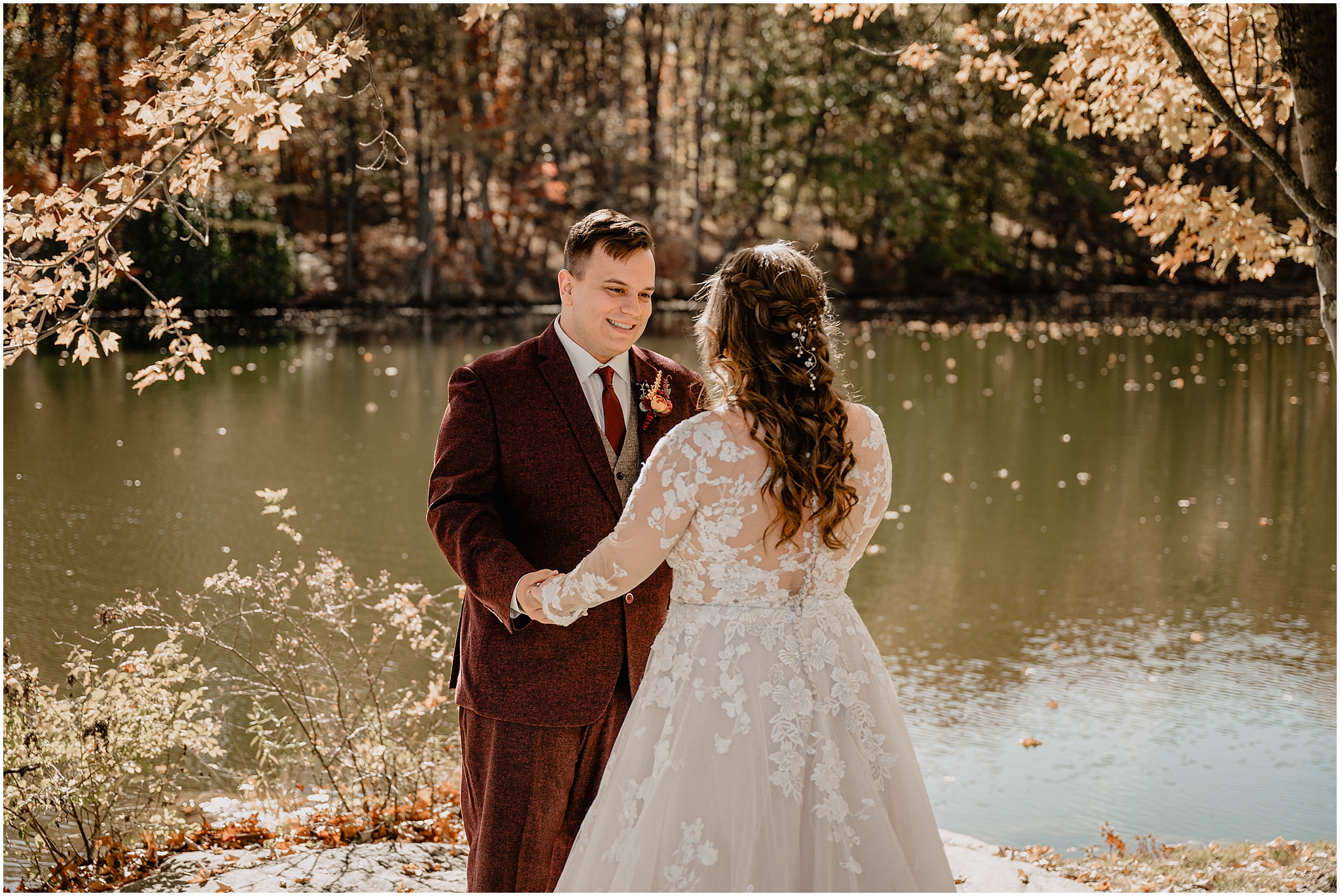 groom in burgundy suit smiles at bride during first look on fall wedding day at the Barn at Perona Farms