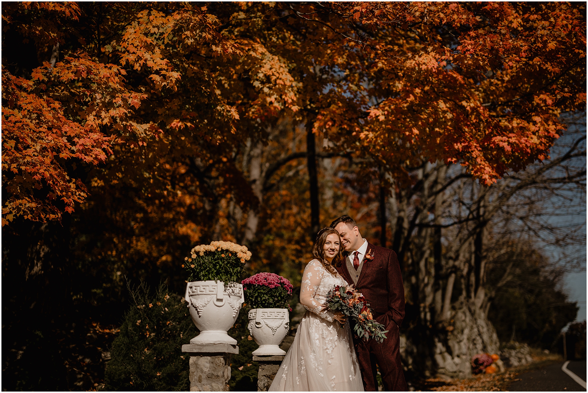 groom leans to hug bride nuzzling her cheek under tree with orange leaves