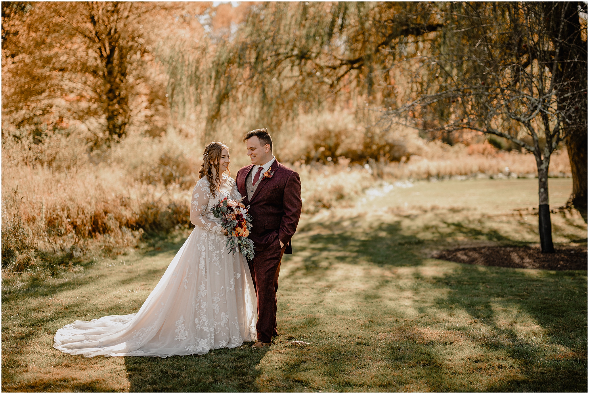 newlyweds hug under willow tree on the lawn at the Barn at Perona Farms