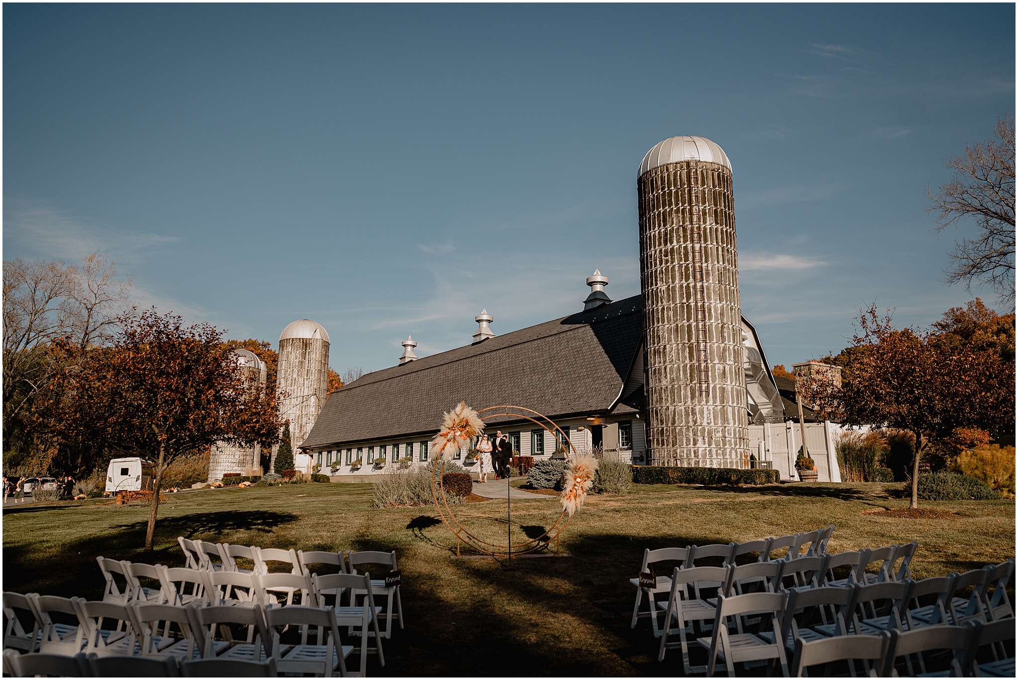 ceremony site with copper circular arch in front of white barn at the Barn at Perona Farms