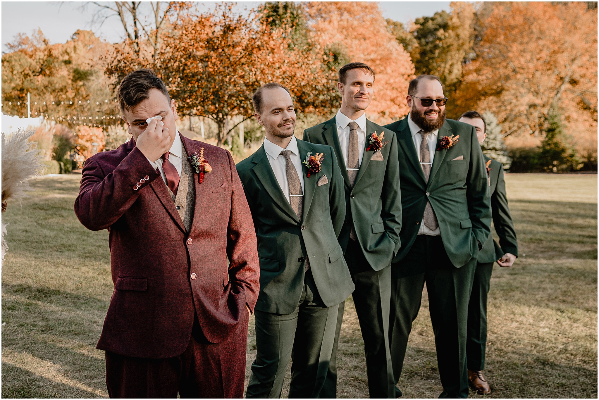 groom wipes away tears during wedding ceremony with groomsmen in emerald suits behind him