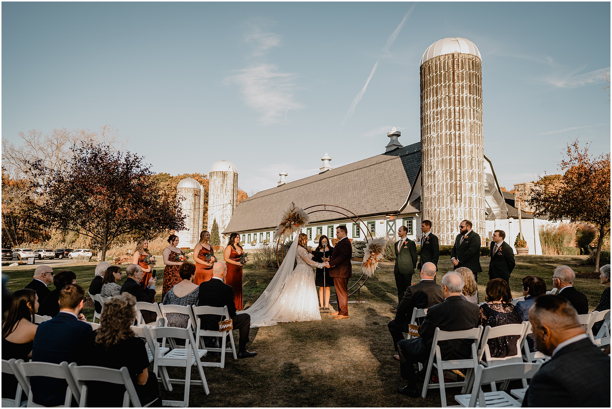 bride and groom hold hands in front of copper circular arbor in front of the Barn at Perona Farms