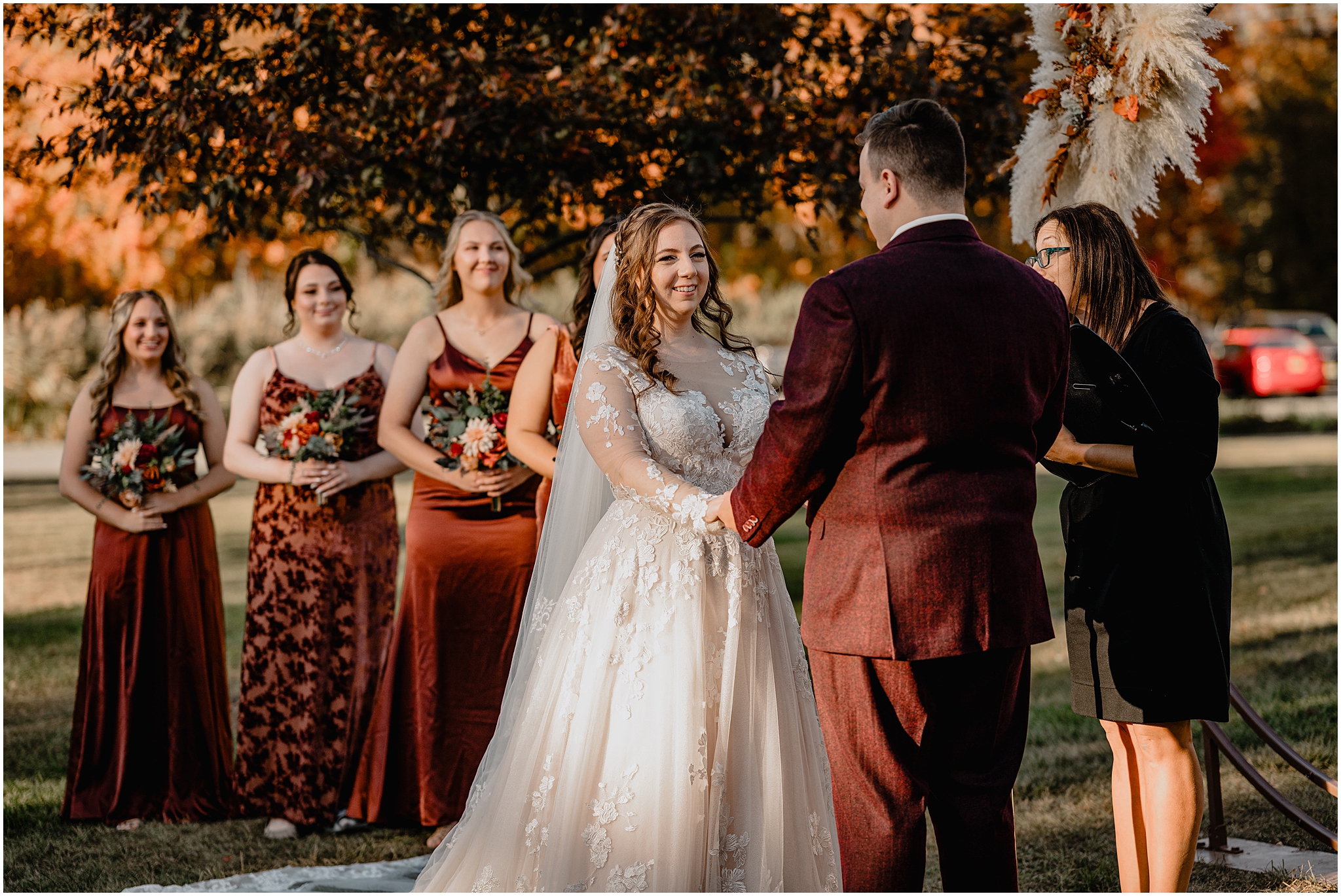 bride and groom hold hands with bridesmaids in burnt orange bridesmaid dresses watching