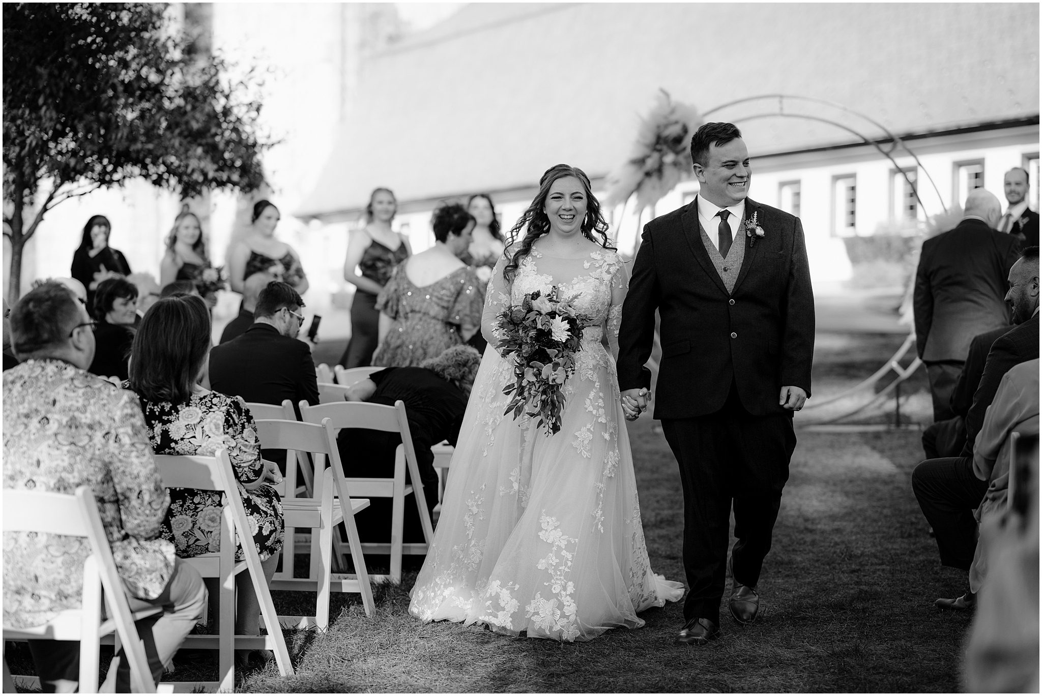 newlyweds hold hands grinning and walking up the aisle at the Barn at Perona Farms