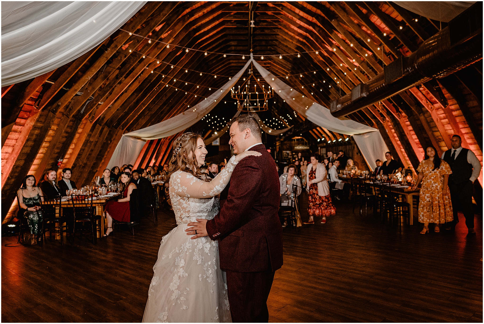 bride dances with groom in burgundy suit inside the Barn at Perona Farms