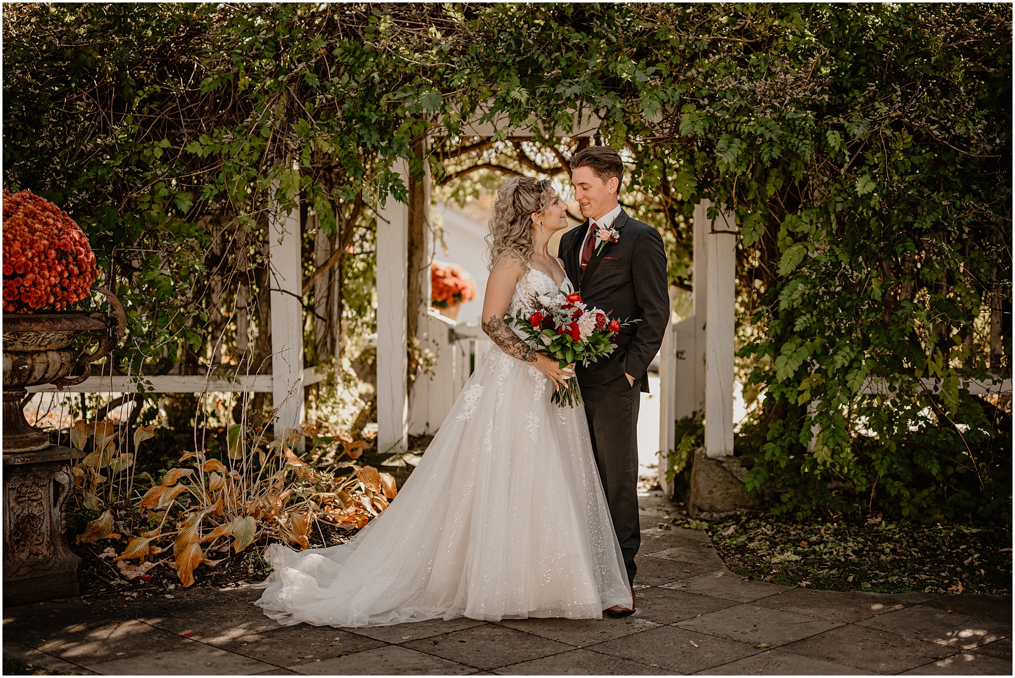 bride smiles up at groom while hugging him under arbor covered in greenery in the Hudson Valley