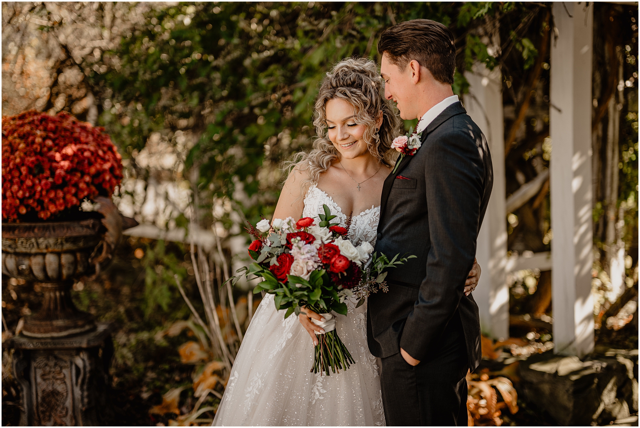 bride hugs groom while looking at bouquet of red and white flowers on fall wedding day in the Hudson Valley