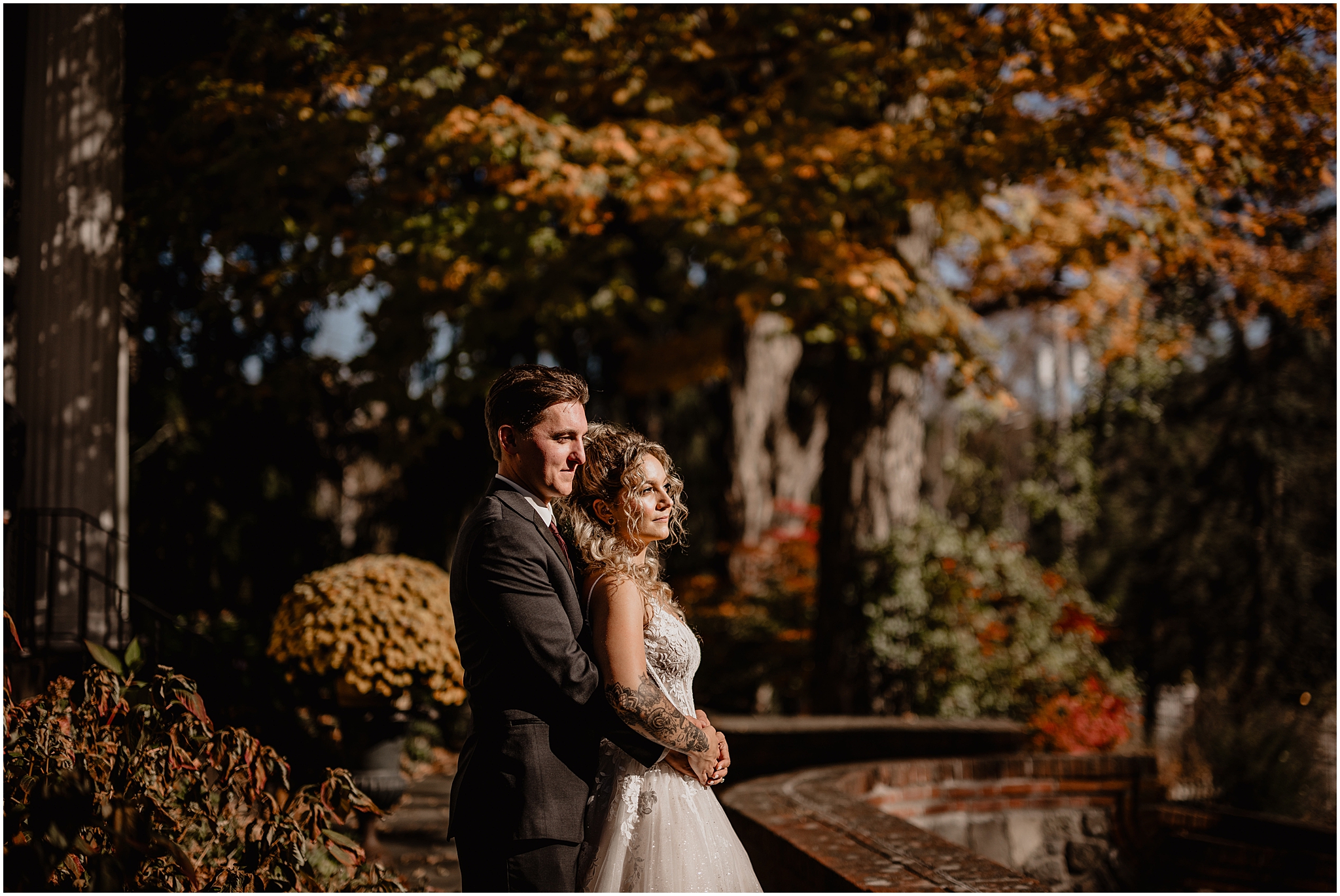 groom hugs bride from behind between brick structures and garden at Hudson Valley wedding venue the Feast at Round Hill