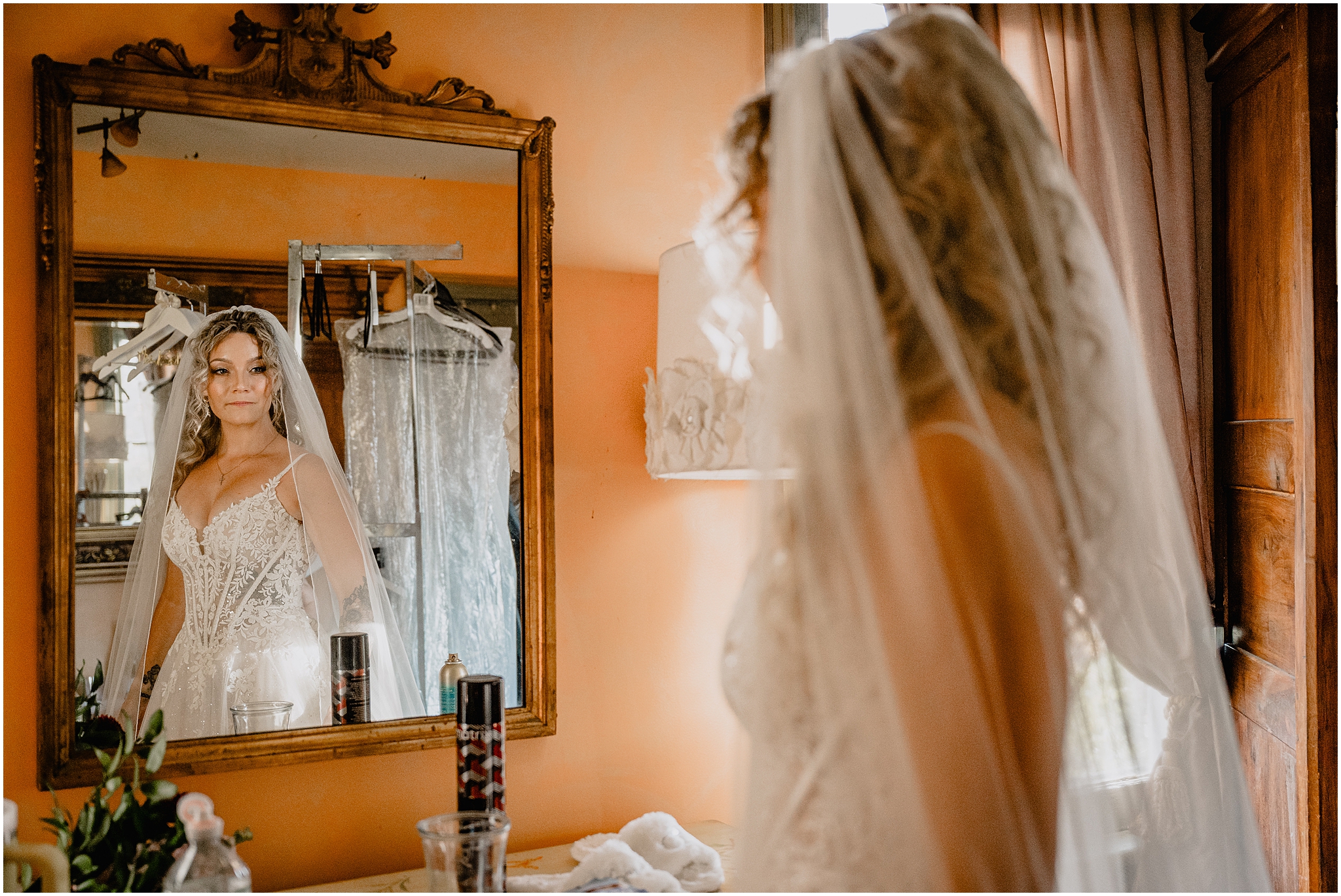bride looks at herself in gold rimmed mirror on orange wall inside the Feast at Round Hill