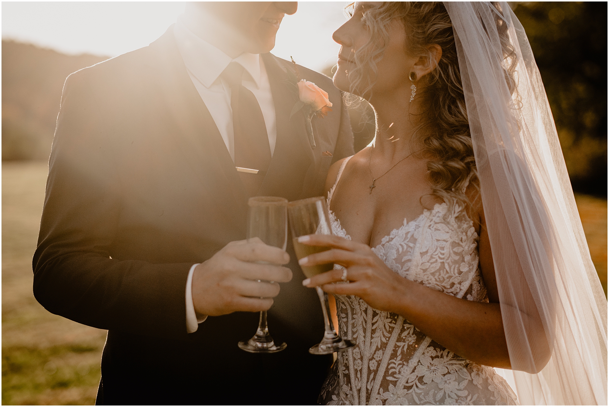 bride and groom toast champagne glasses while smiling at each other at sunset 