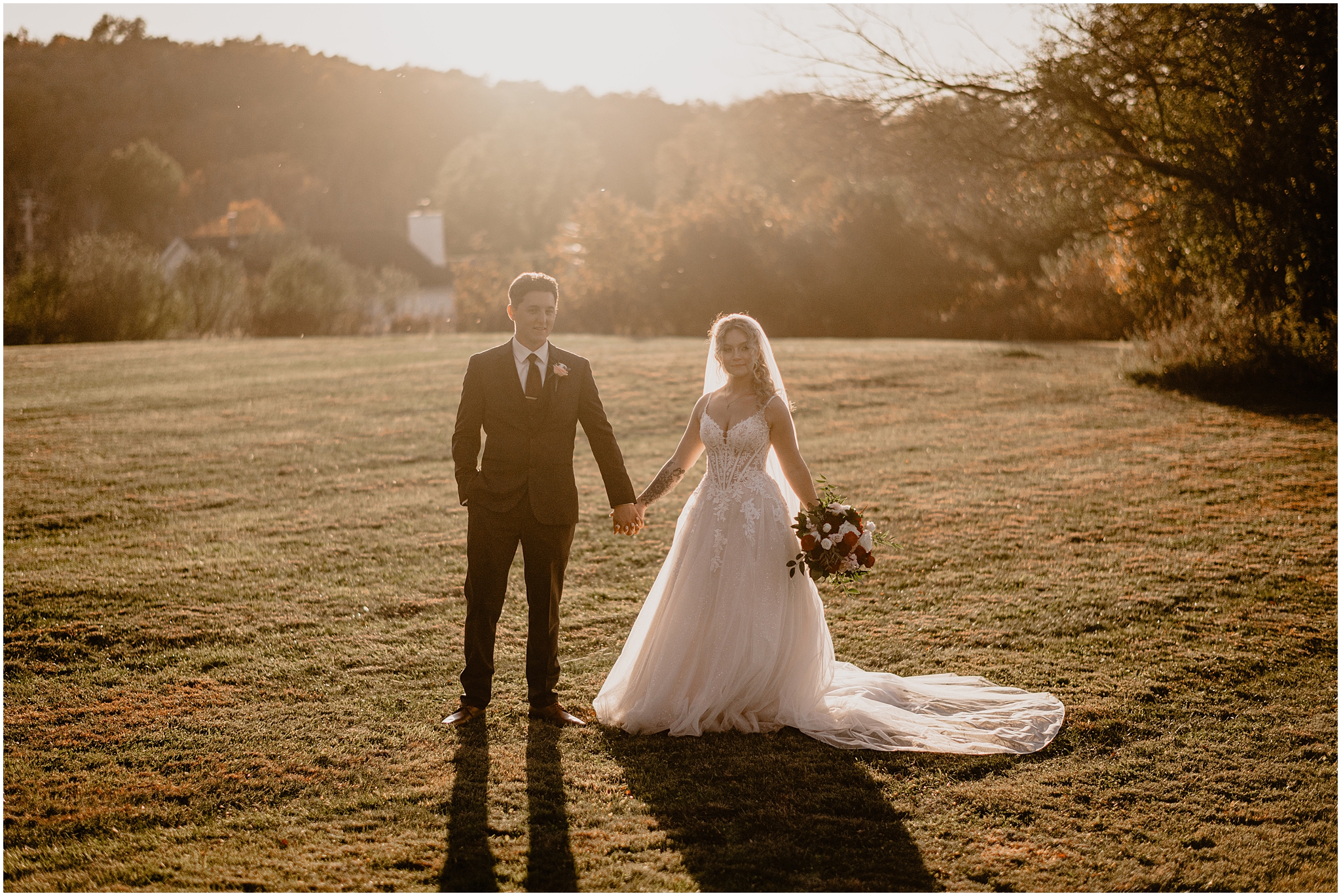 groom holds hands with bride holding bouquet of red and white flowers on lawn of Hudson Valley wedding venue 