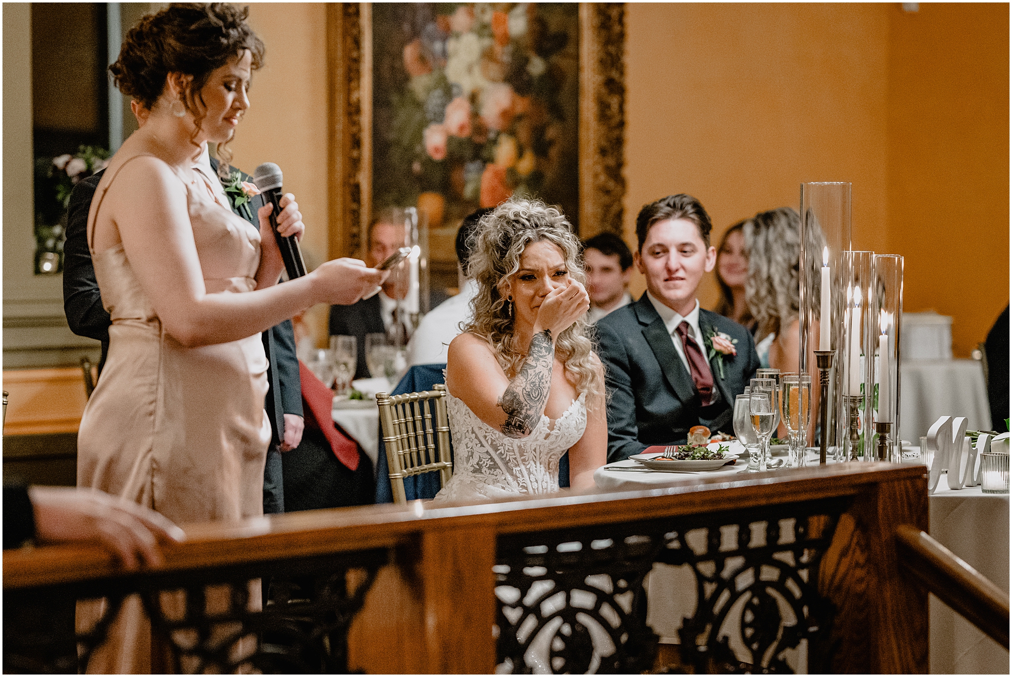 bridesmaid gives speech while bride cries sitting at table with groom