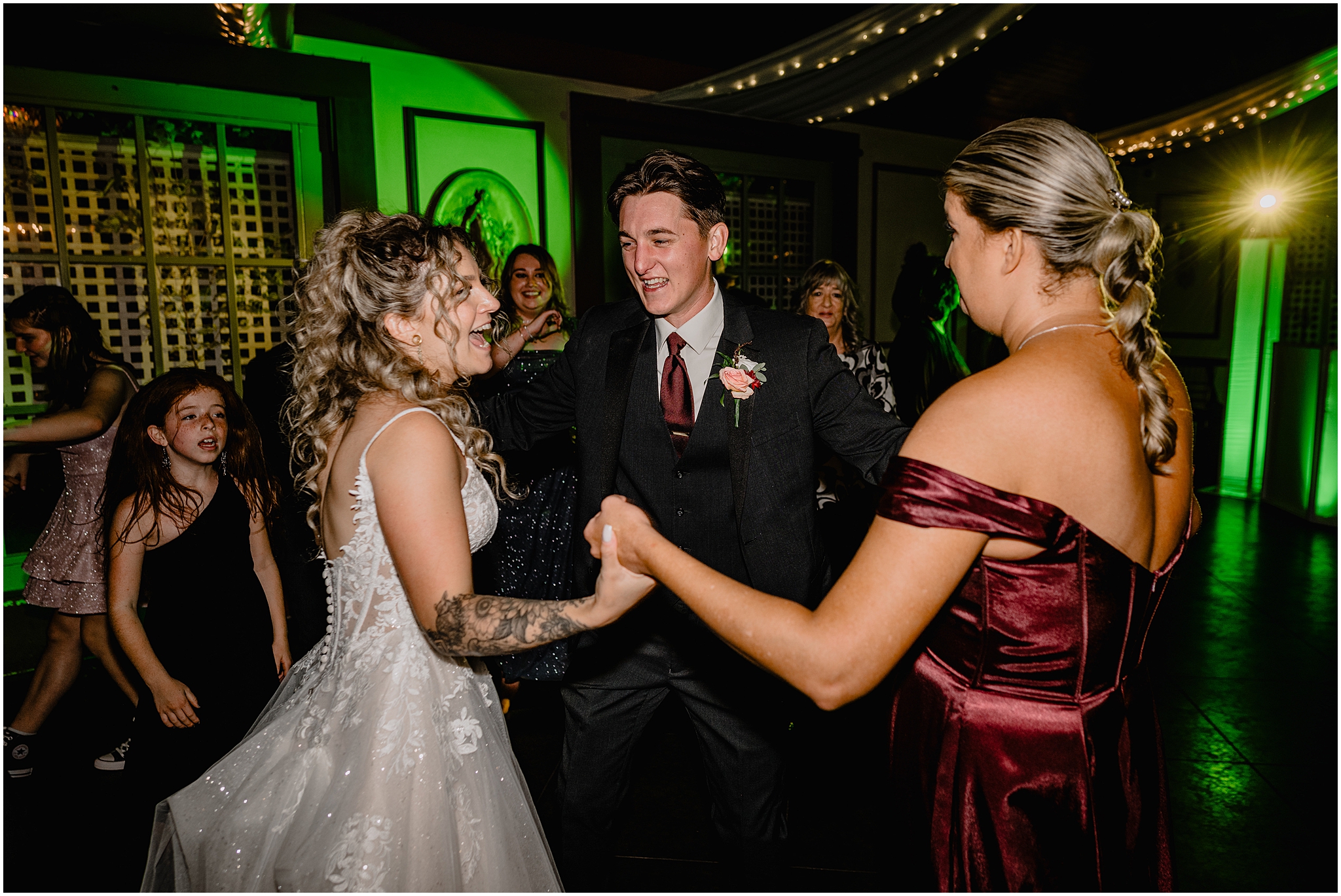 bride and groom hold hands dancing with bridesmaid in red gown during wedding reception at the Feast at Round Hill