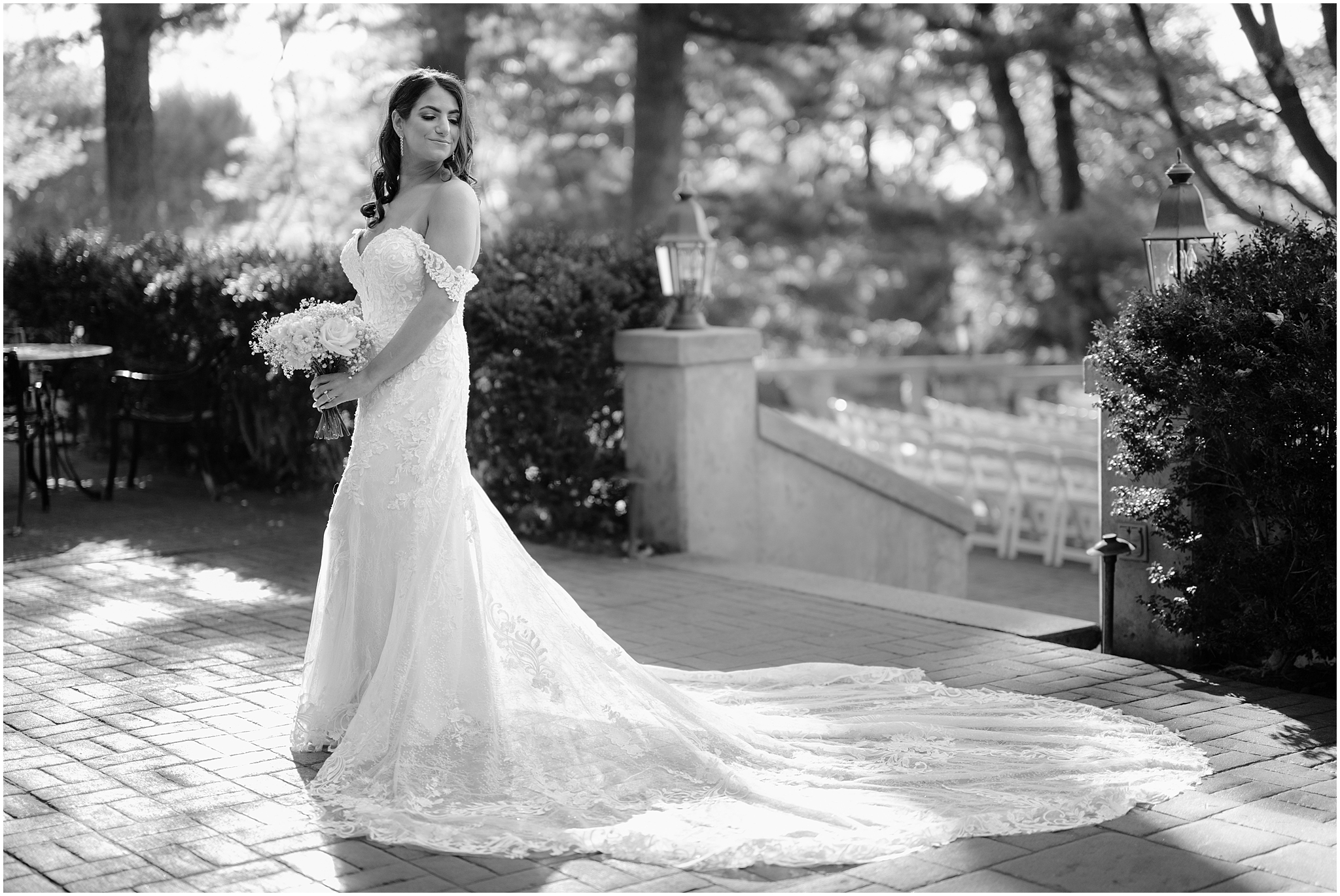 bride holds bouquet of white roses and baby's breath standing on brick patio outside Tappan Hill Mansion