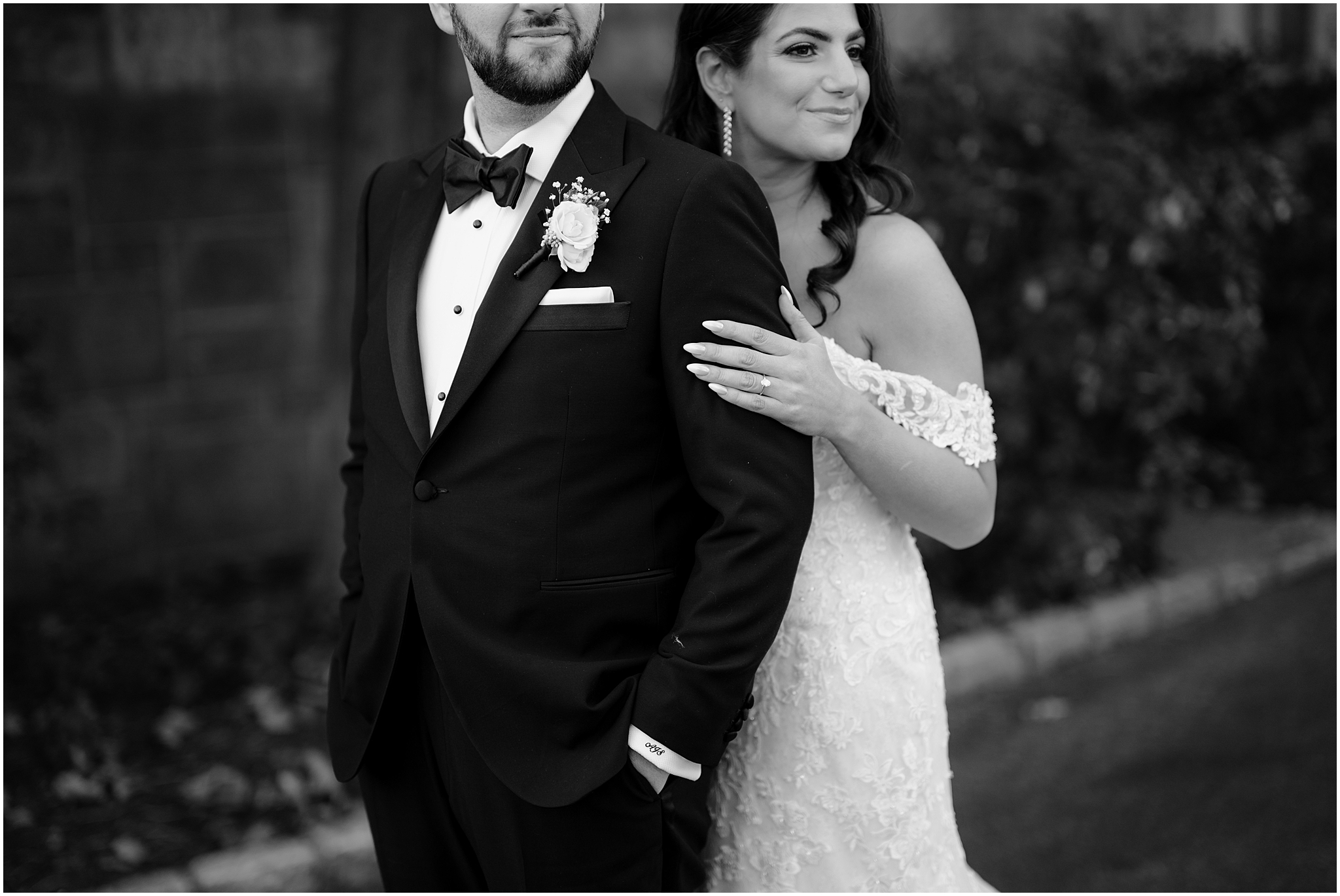 bride holds groom's arm from behind showing off engagement ring 