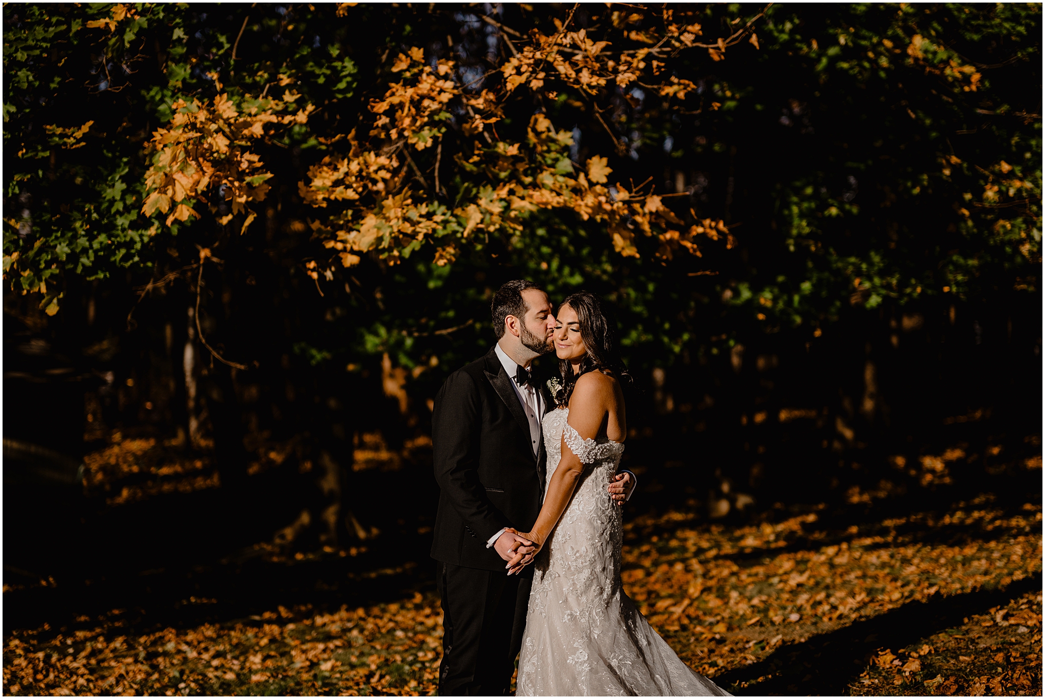 bride and groom hold hands while groom kisses bride's cheek in front of orange leaves at Tappan Hill Mansion